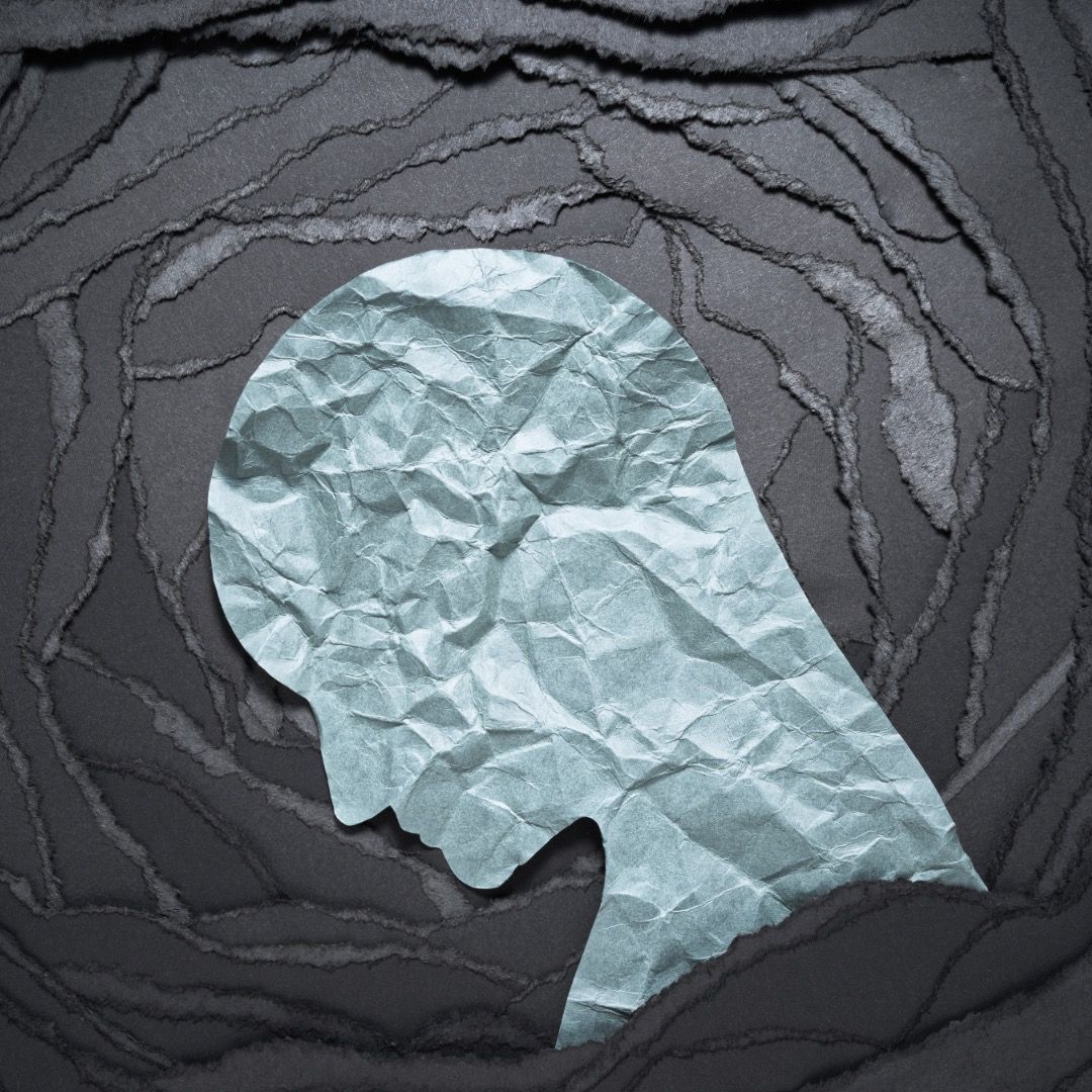 Silhouette profile made of crumpled light blue paper against dark textured background showing mental health concept.