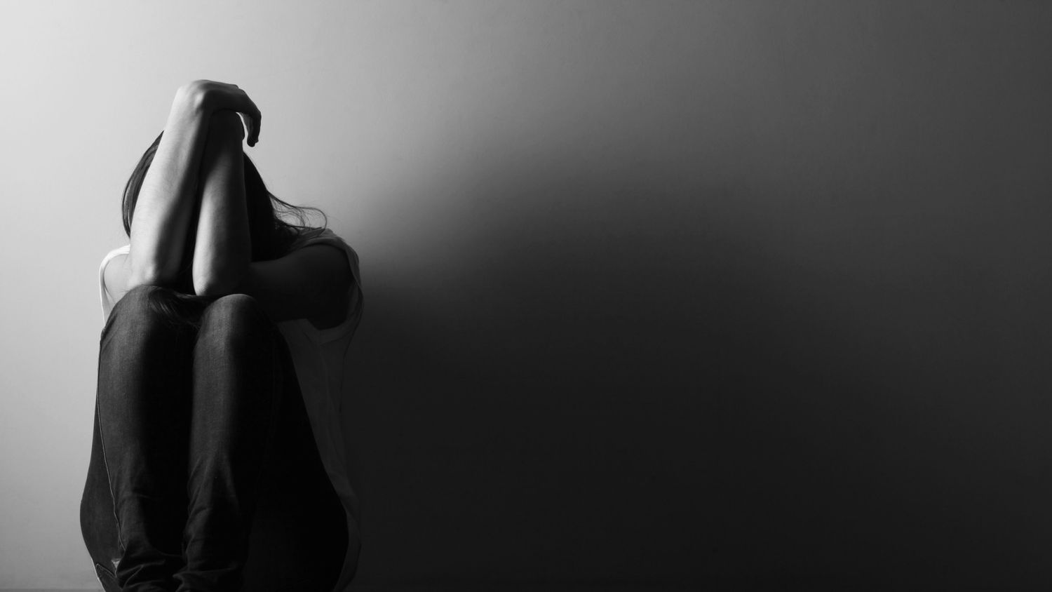 A silhouetted figure sits alone in darkness, creating a moody black and white artistic composition.