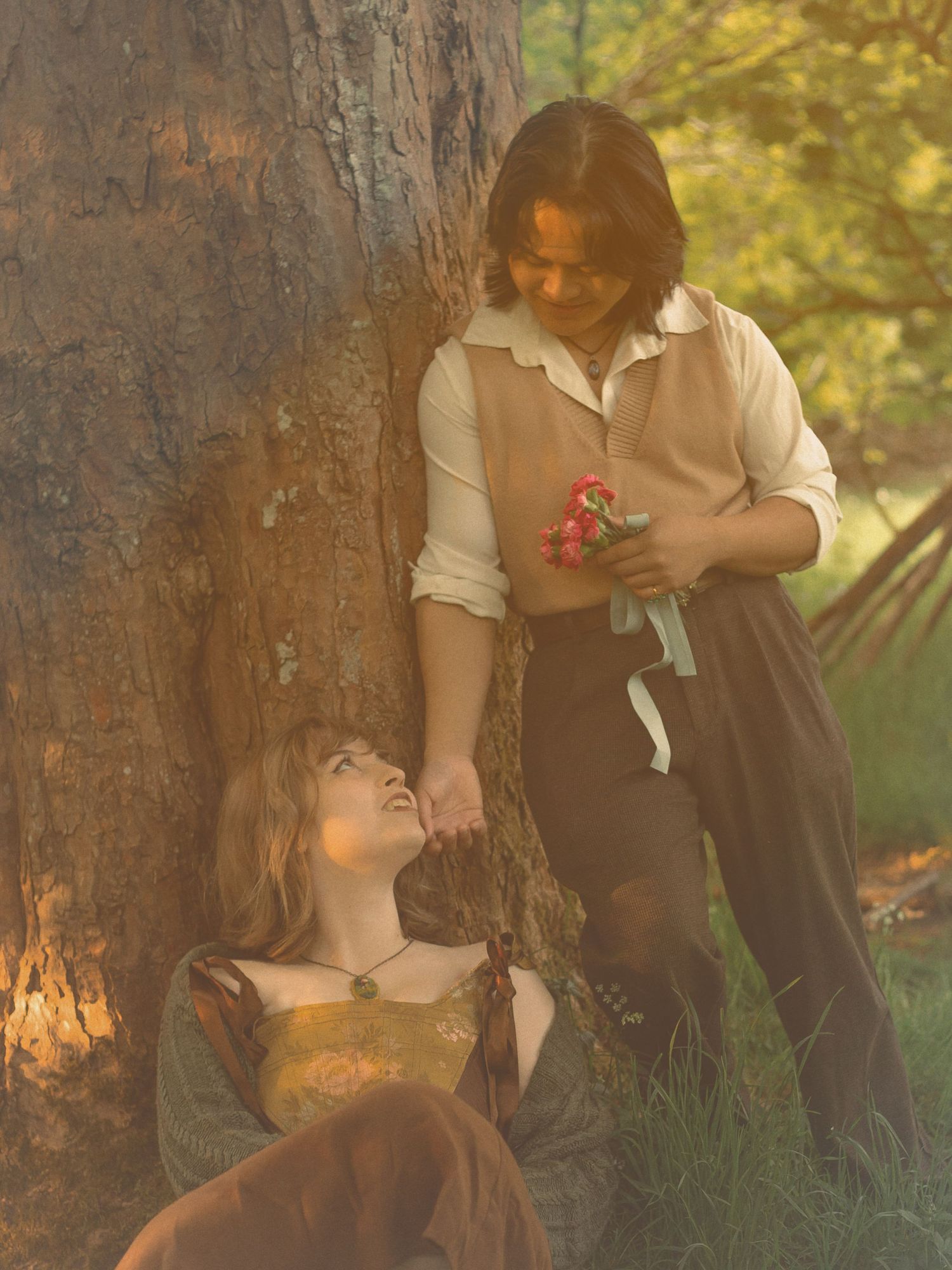 young-couple-gazing-at-eachother-lovingly-wearing-vintage-style-clothing-and-holding-flowers-under-a-tree