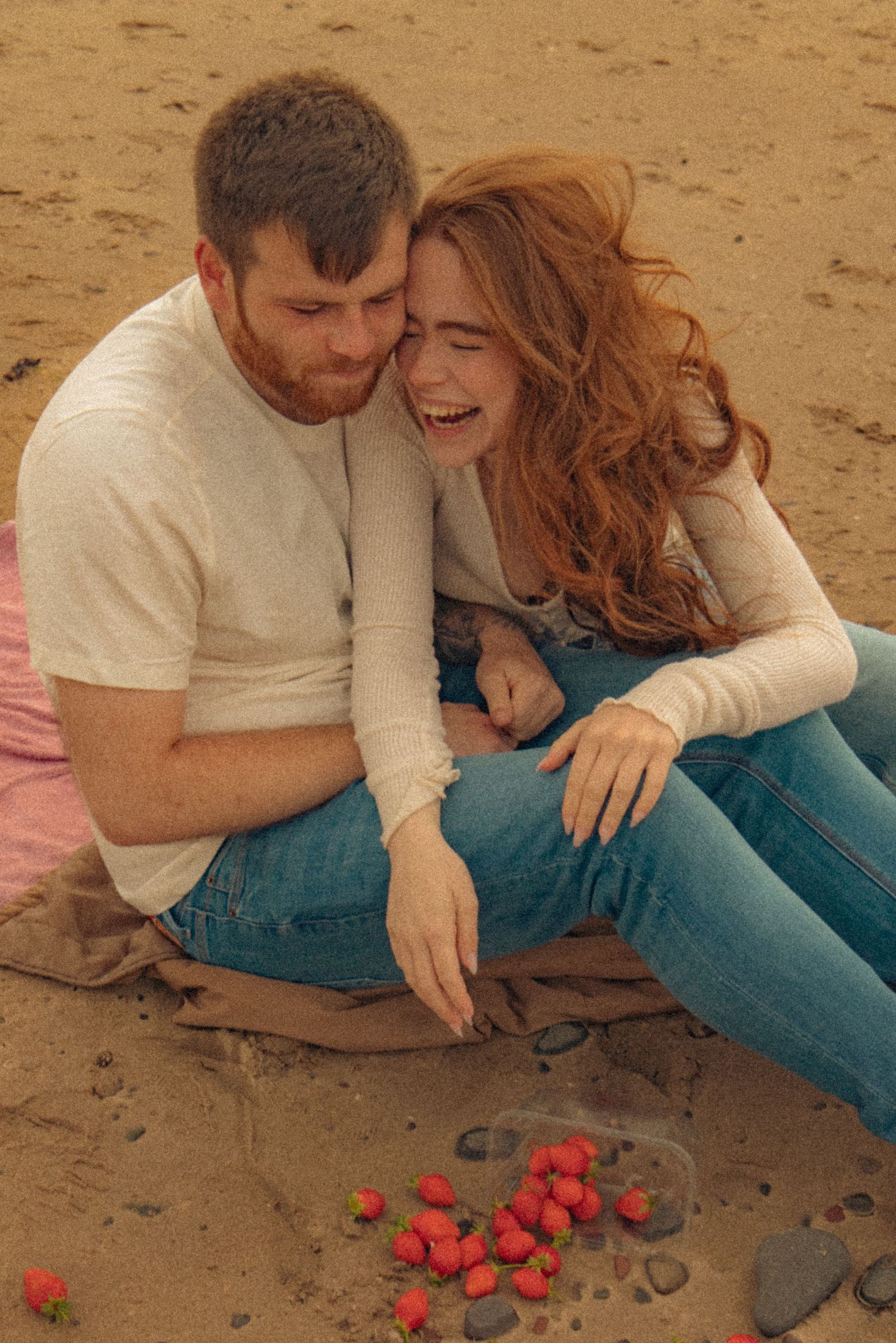 couple-laughing-on-the-beach-whilst-having-a-picnic