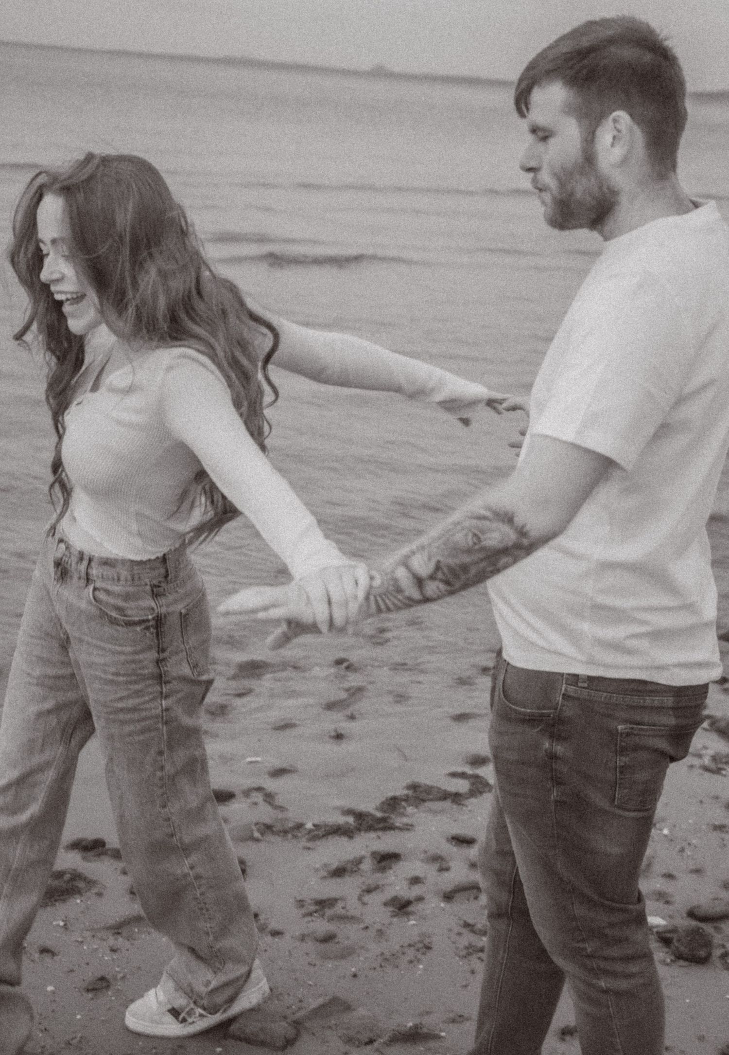 young-couple-playing-on-the-beach-candid-b&w-photo