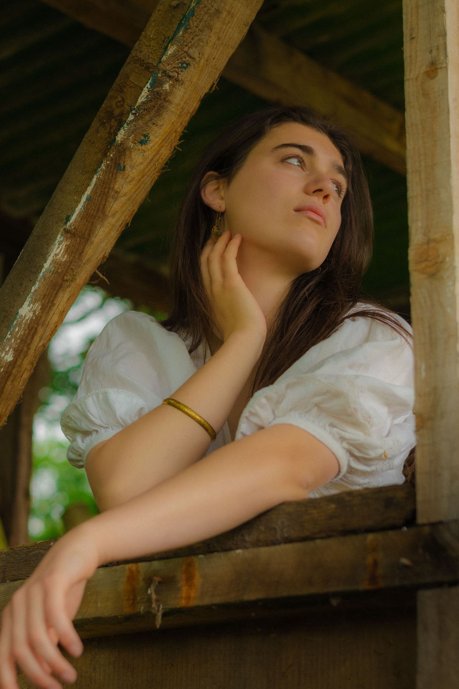 Artistic portrait under wooden beams wearing a white vintage-style dress.