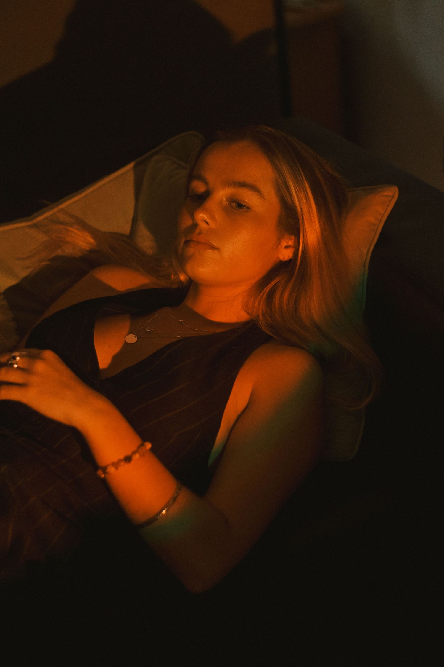 Person reclining on couch in dark room with amber lighting.