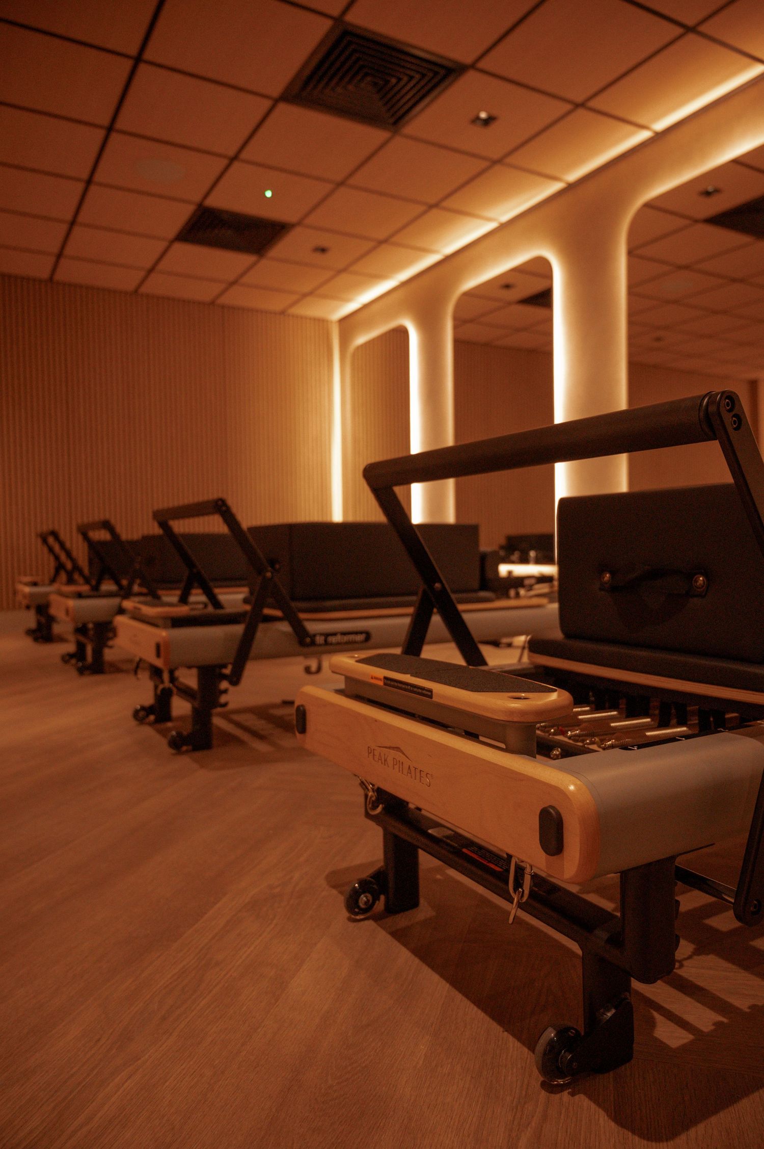 Luxury Pilates reformer studio with warm amber lighting, wood floors, and a row of modern reformer machines.