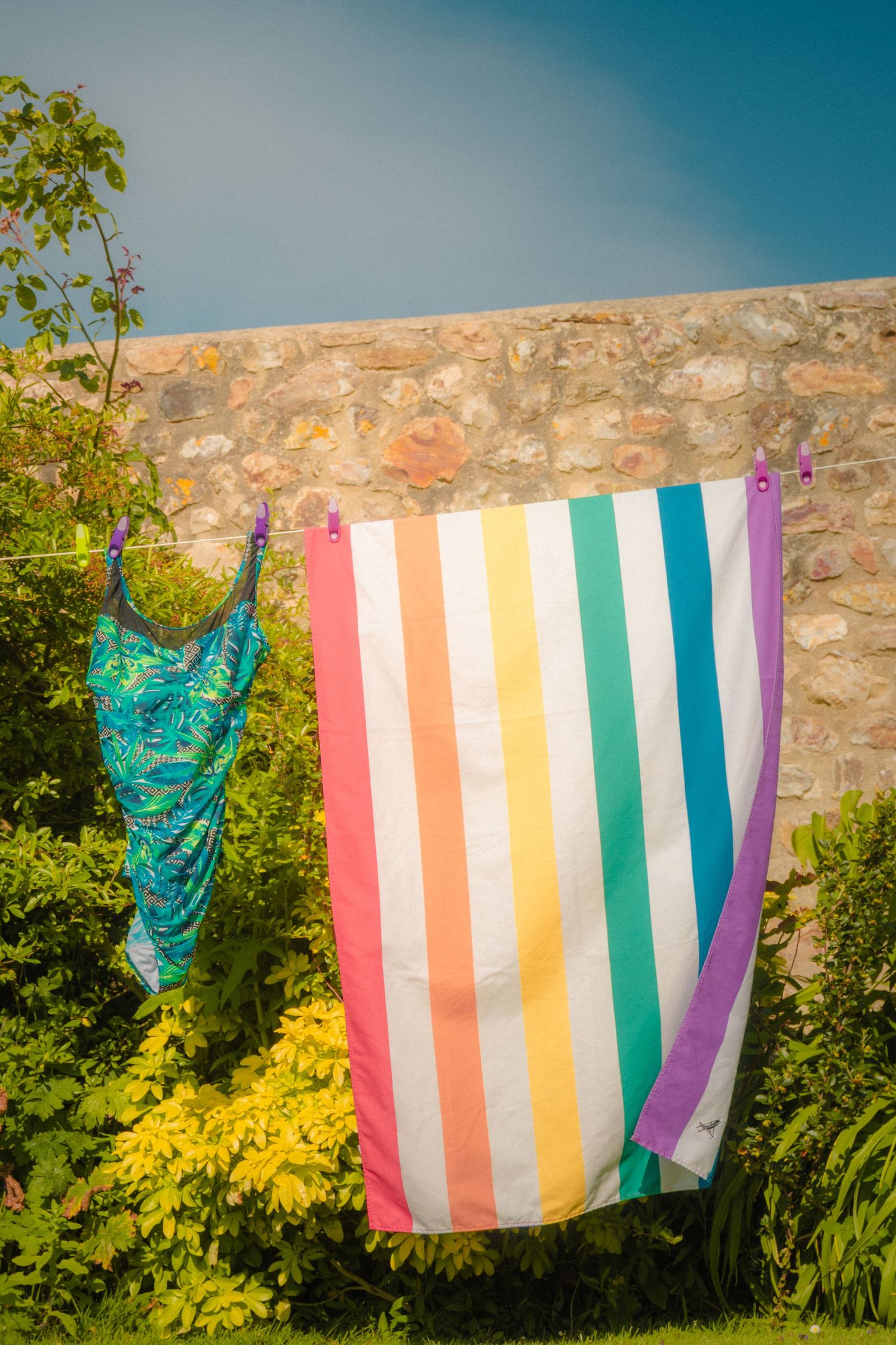 Colorful striped laundry hanging to dry on a stone wall against a blue sky.