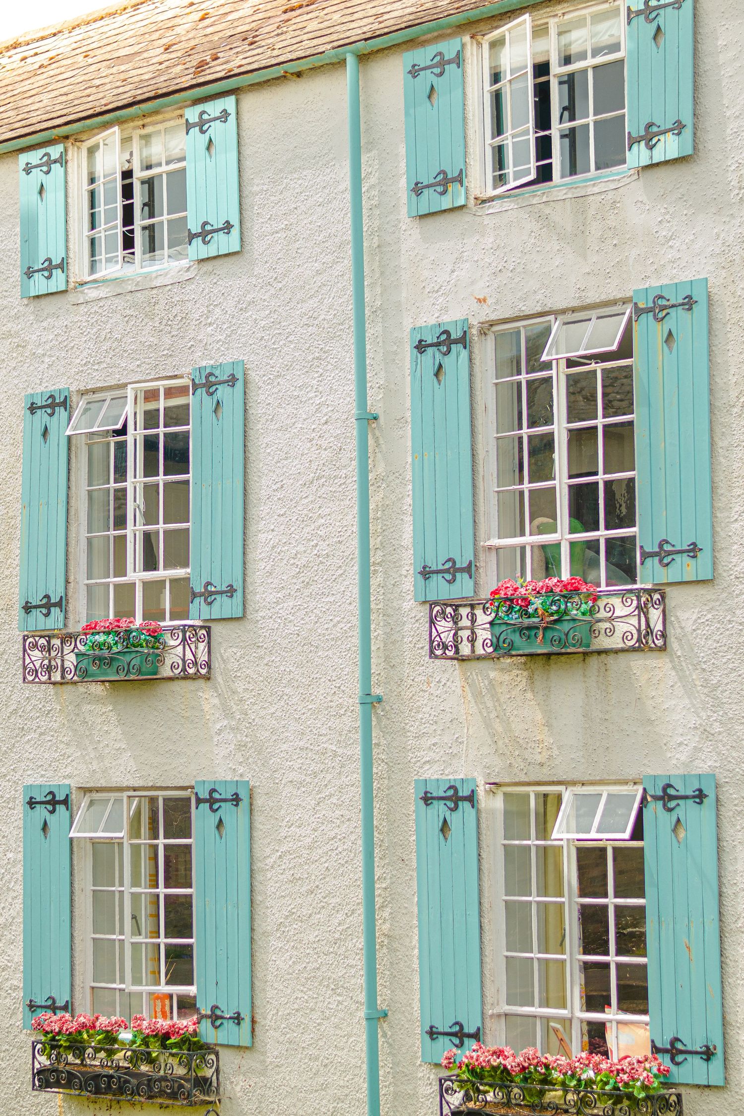 White building facade with mint green shutters and window boxes filled with pink flowers.