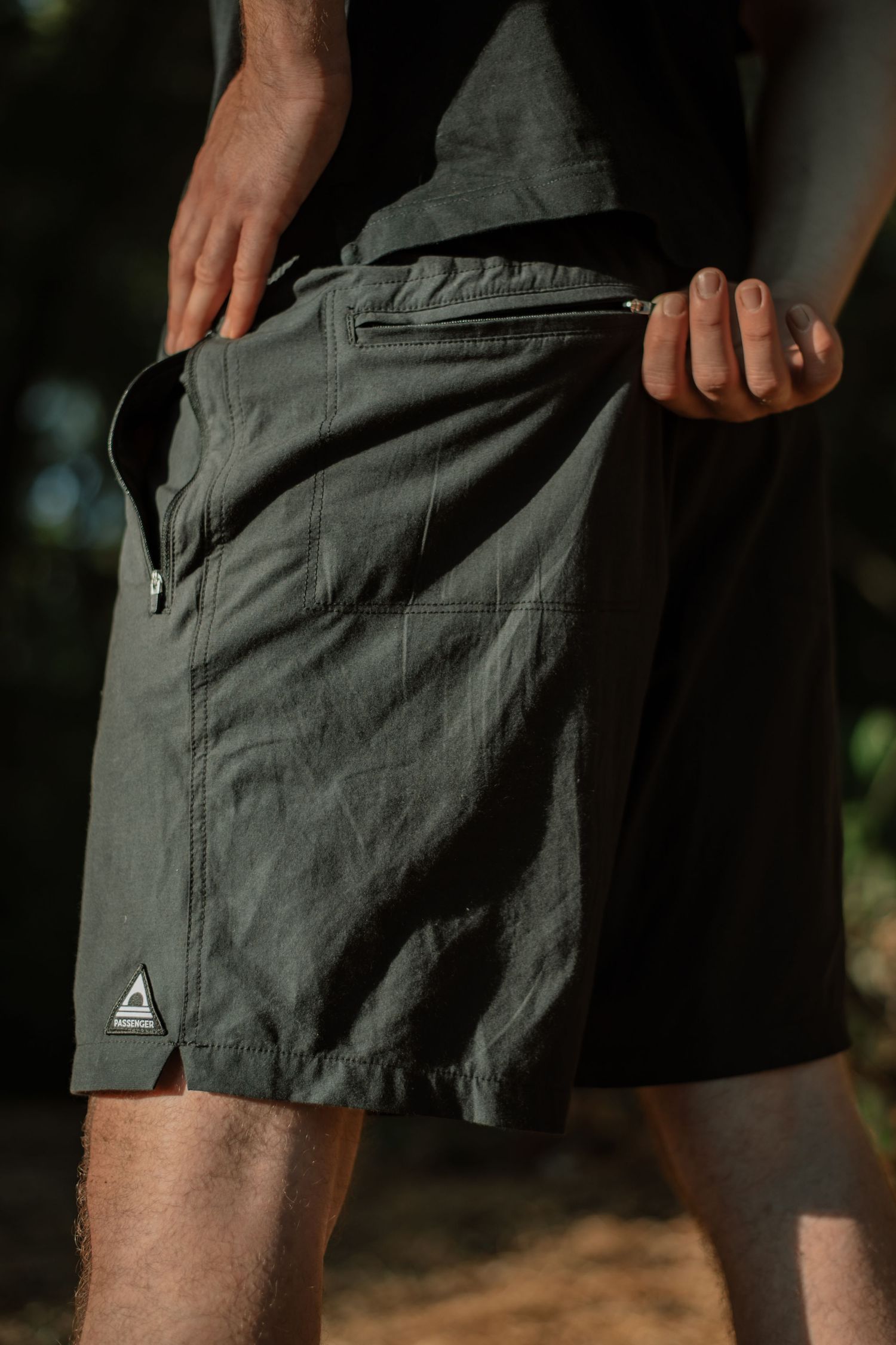 Man wearing olive green cargo shorts with zipper pocket detail, shown from waist down in outdoor setting.
