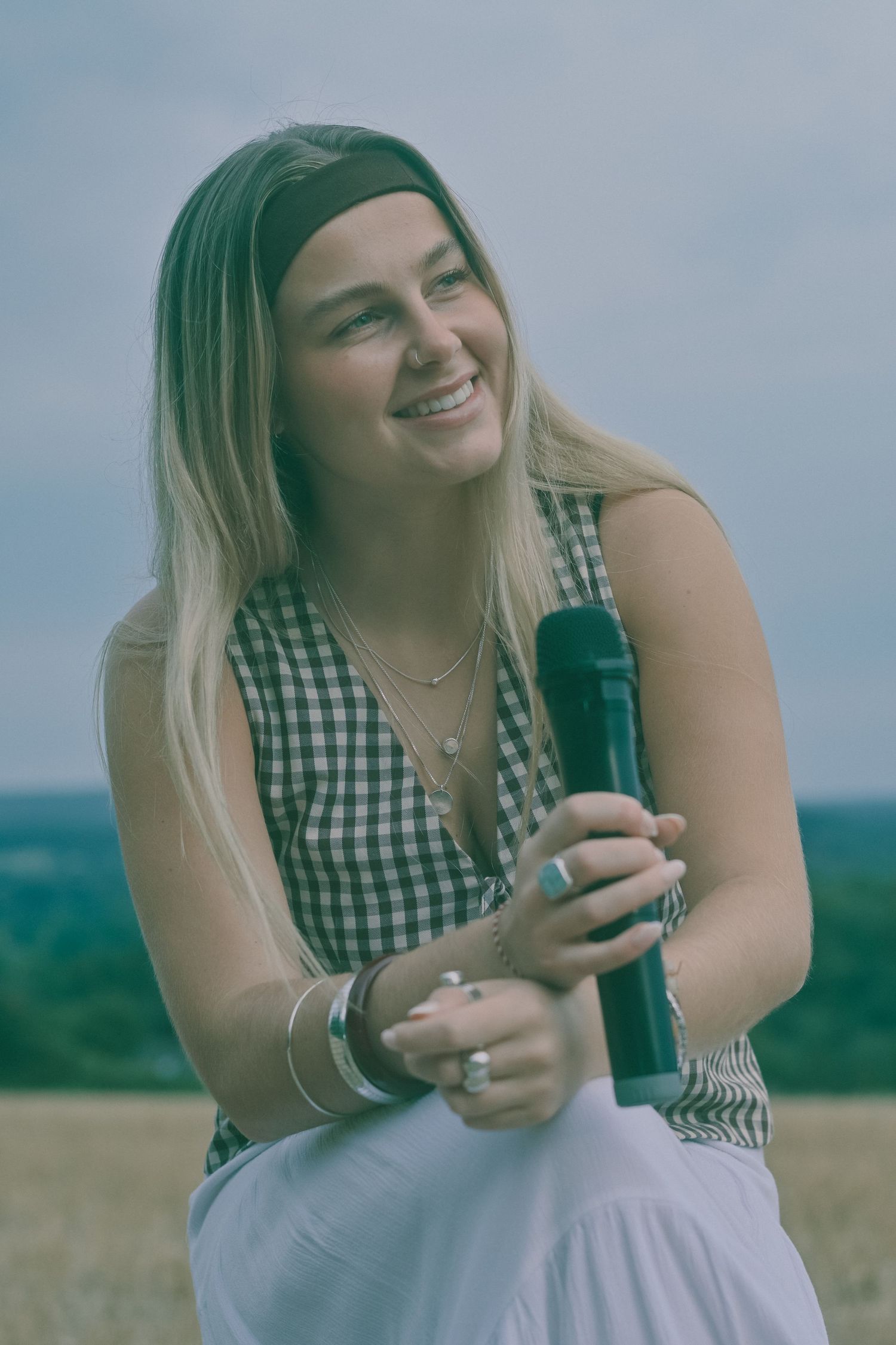 Person in gingham top holding a microphone outdoors with soft natural lighting.