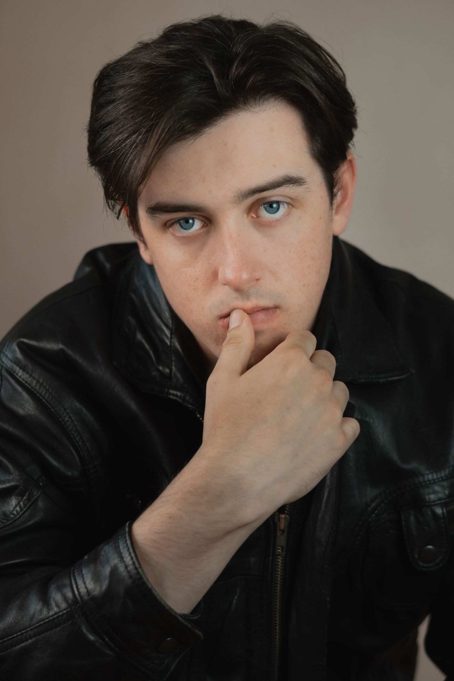 Moody portrait series in leather jacket with contemplative poses against gray background.