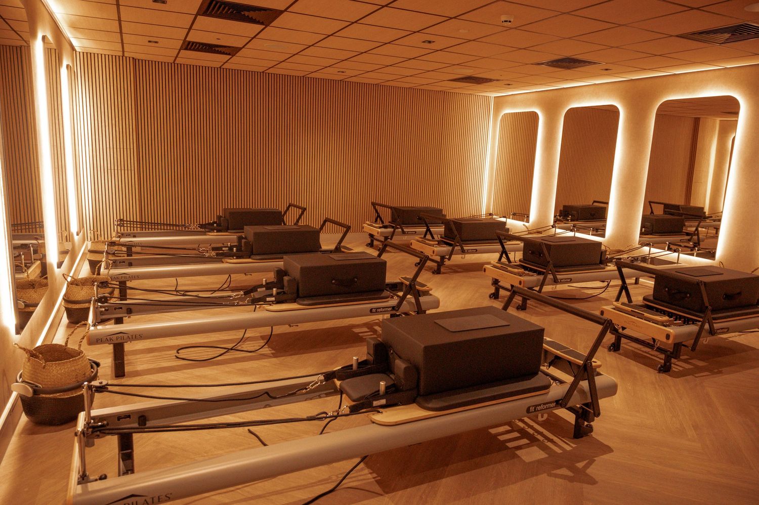 Pilates studio with multiple reformer machines arranged in rows, warm amber lighting, and elegant arched mirrors on the wall.