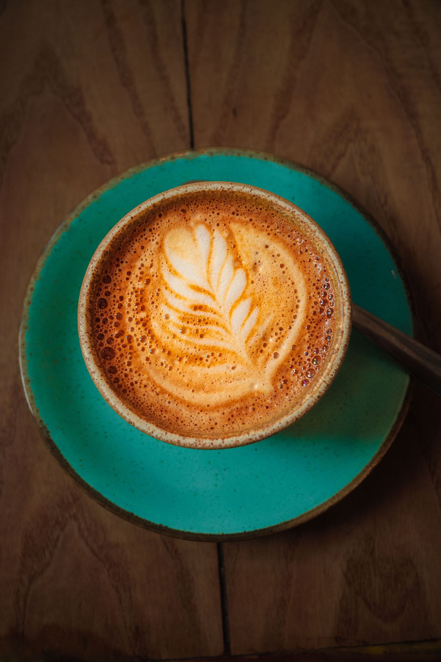Latte art in a turquoise ceramic cup showing intricate leaf pattern design.