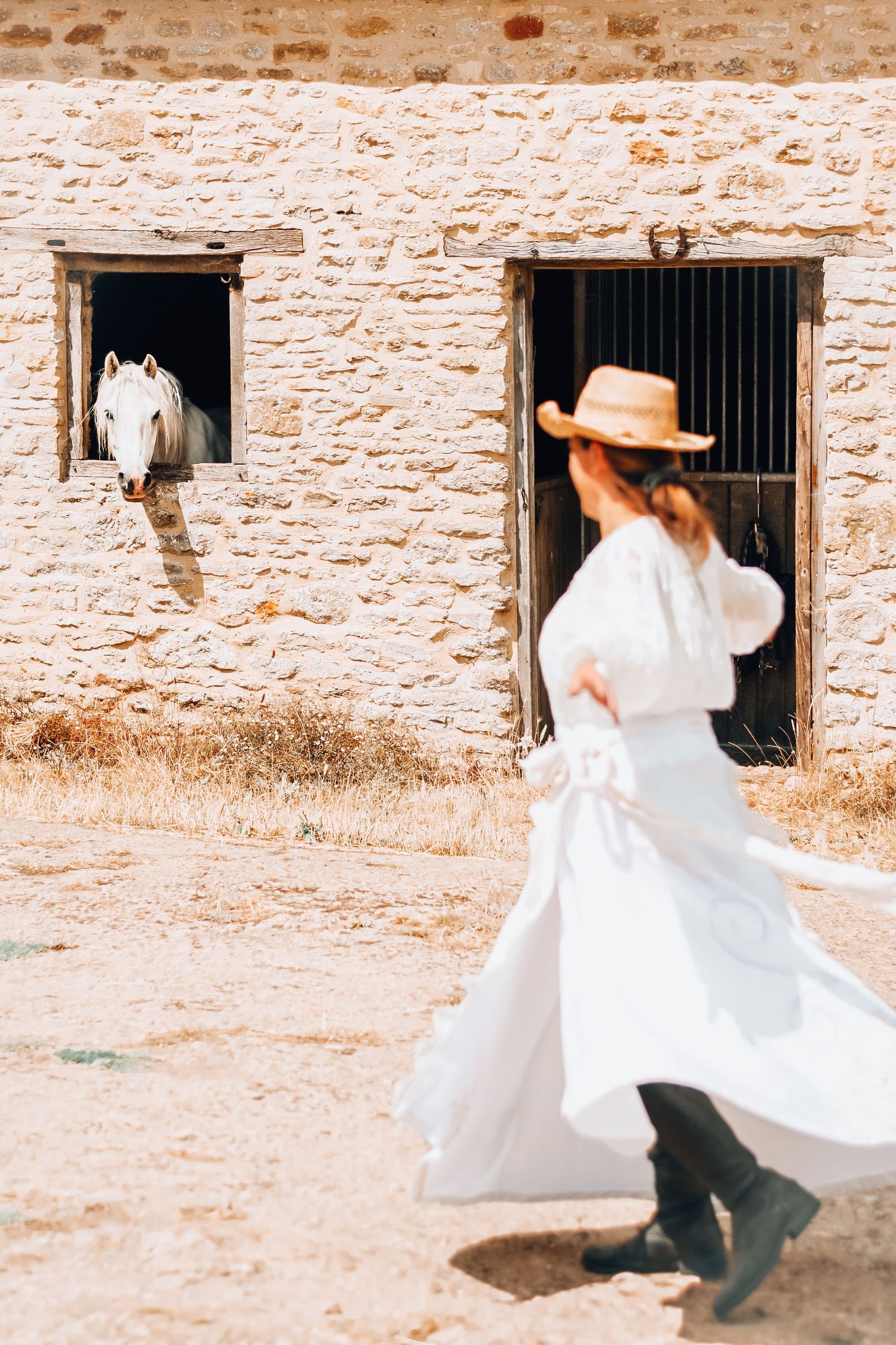 White-dressed figure dances carefree in front of an old stone building with barred windows.