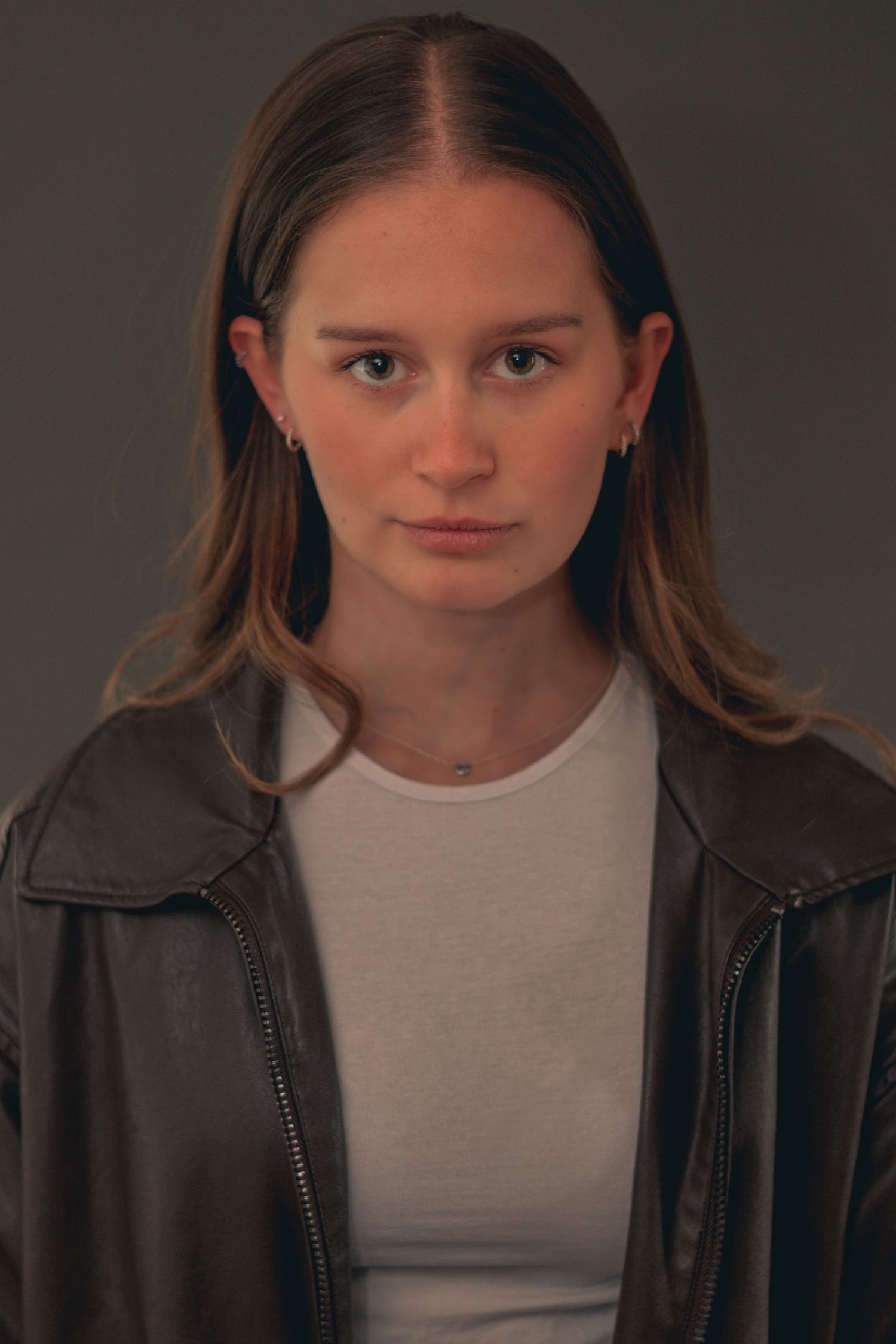 Portrait series against dark background wearing leather jacket and white top.