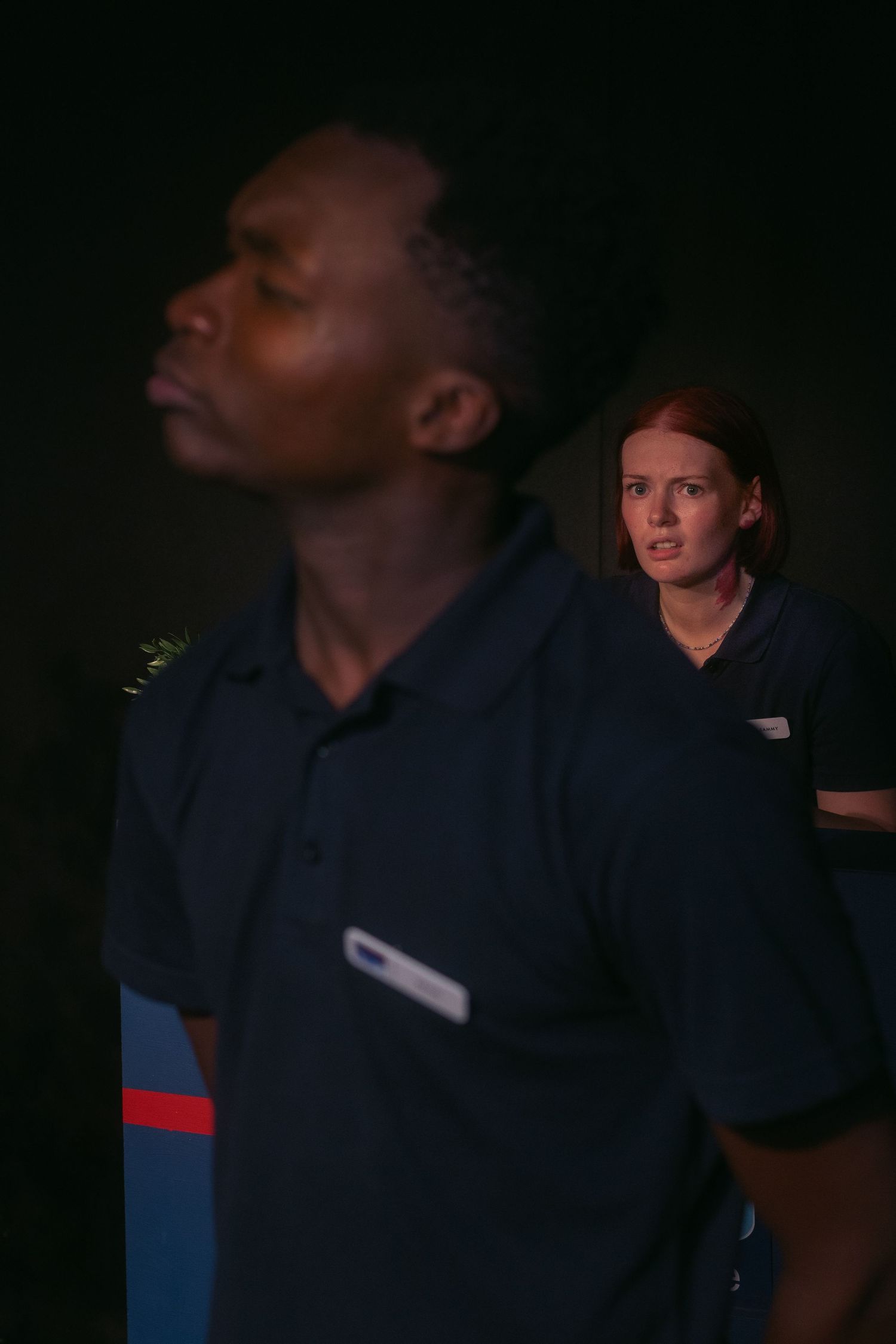 Staff members in dark uniforms standing near a branded counter in low light.