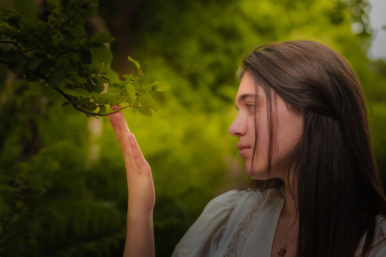 Side profile with flowing hair against verdant forest background in natural light.