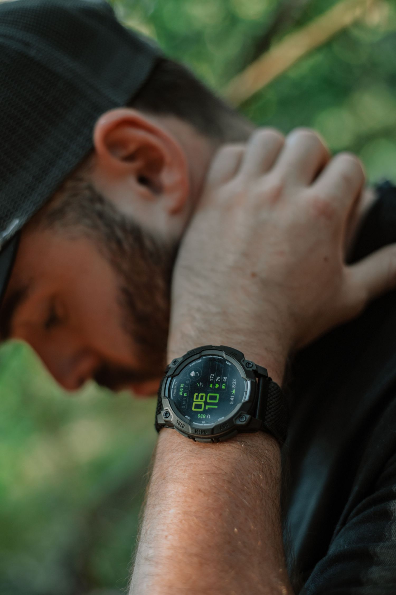 Bearded man wearing a black digital tactical watch with green display, outdoors in a forest setting.