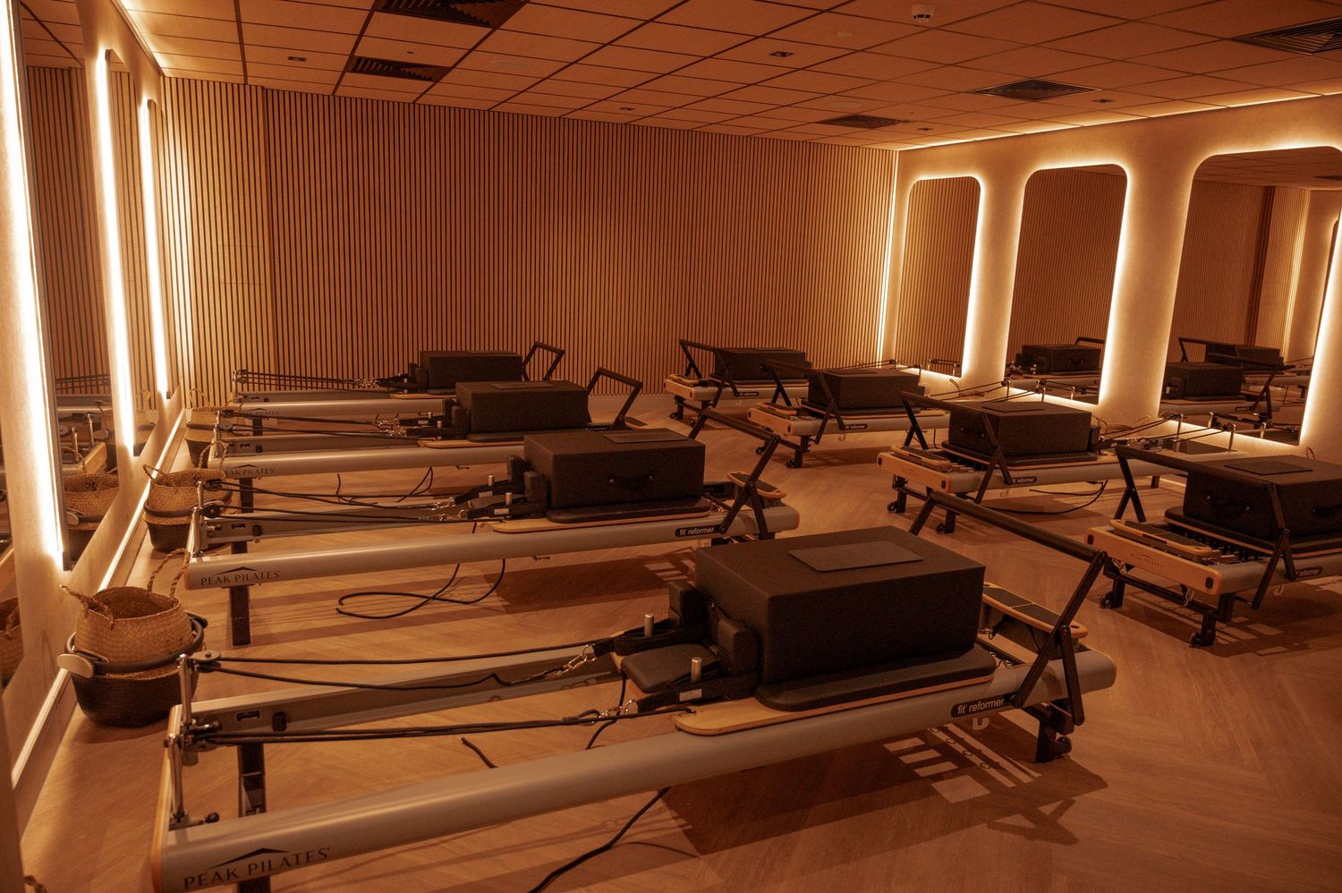 Pilates reformer studio with warm amber lighting, multiple reformer machines, and elegant arched mirrors along the walls.