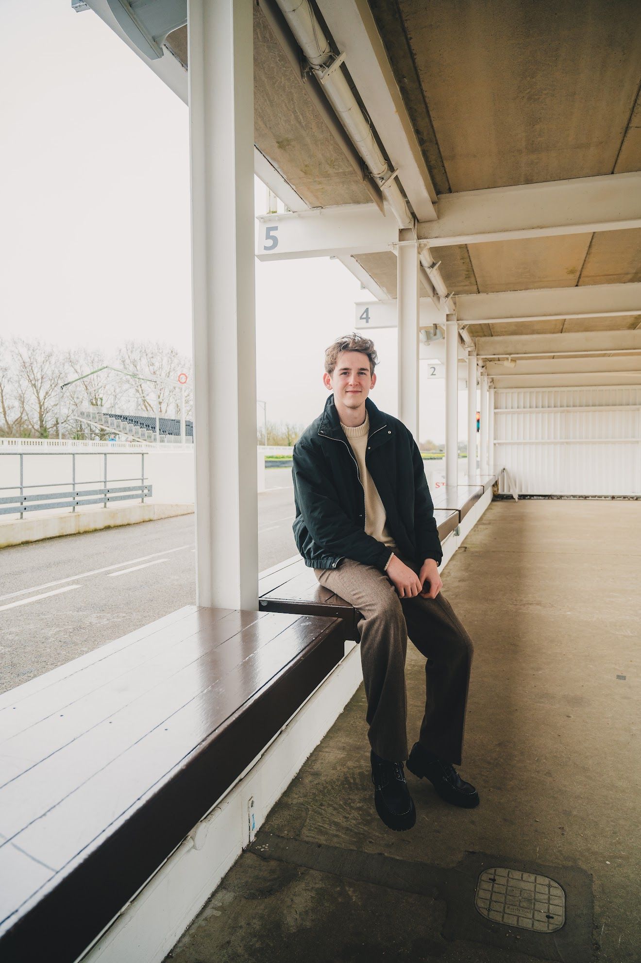 Person sitting on wooden bleachers in an empty covered area with white support columns.