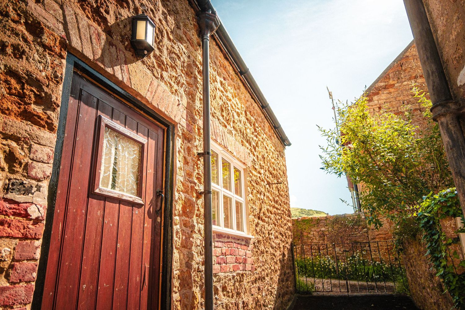 Stone cottage exterior with burgundy trim and windows capturing warm sunlight.