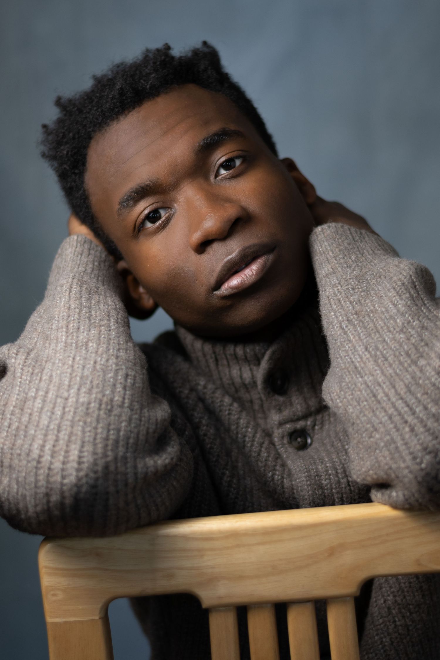 Cozy portrait wearing a grey turtleneck sweater while resting on wooden furniture.