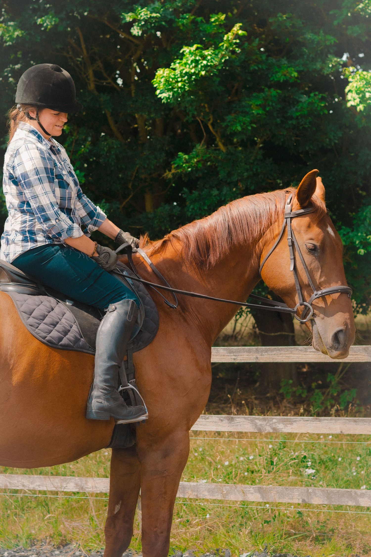 Rider wearing safety helmet mounted on chestnut horse near wooden fence.