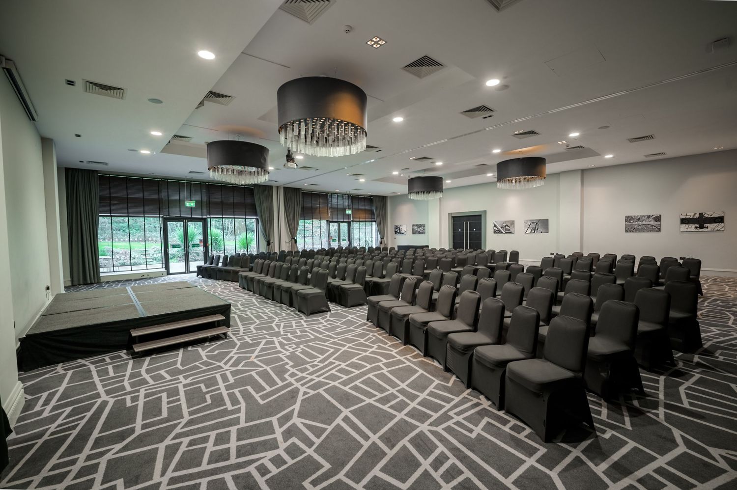 Elegant conference room with rows of black chairs, patterned carpet, and modern pendant lights in a spacious venue.