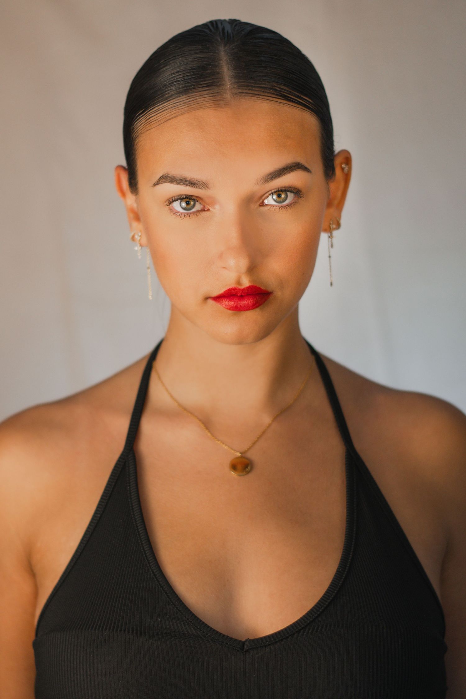 Studio beauty shot featuring dark tank top, red lipstick and delicate gold necklace.
