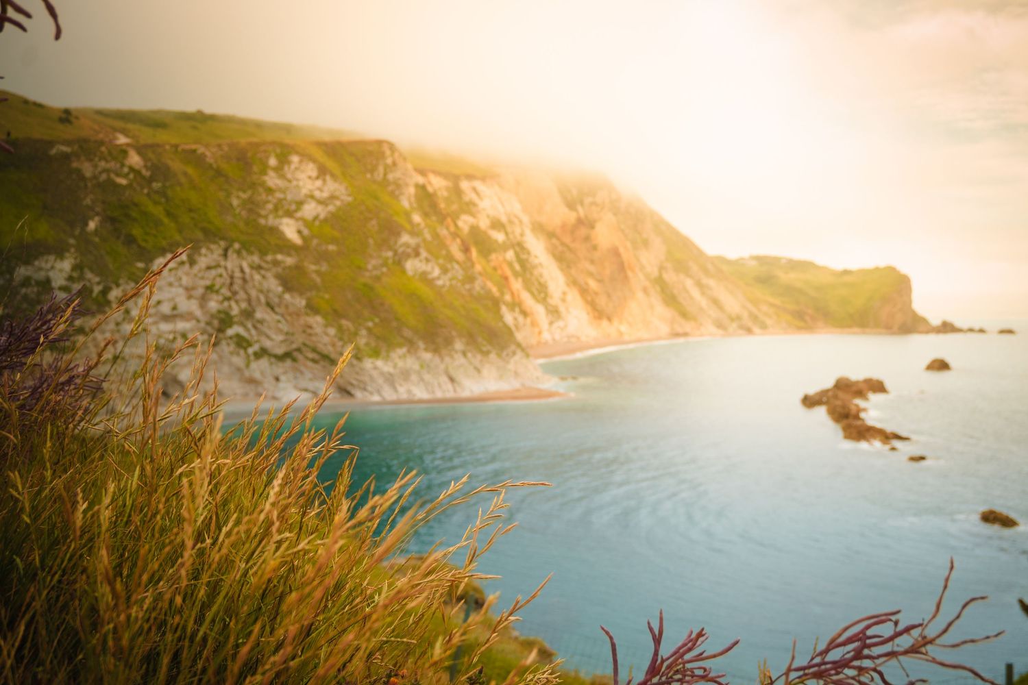 Dramatic sunset over coastal cliffs with golden light reflecting on ocean waters.