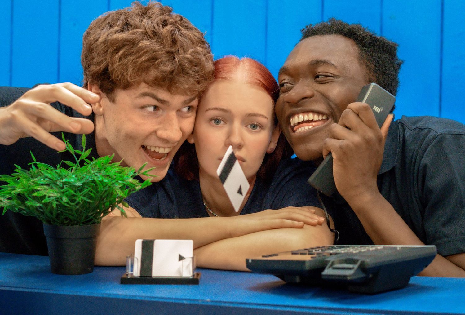Friends sharing laughs while looking at mobile phones against bright blue background.