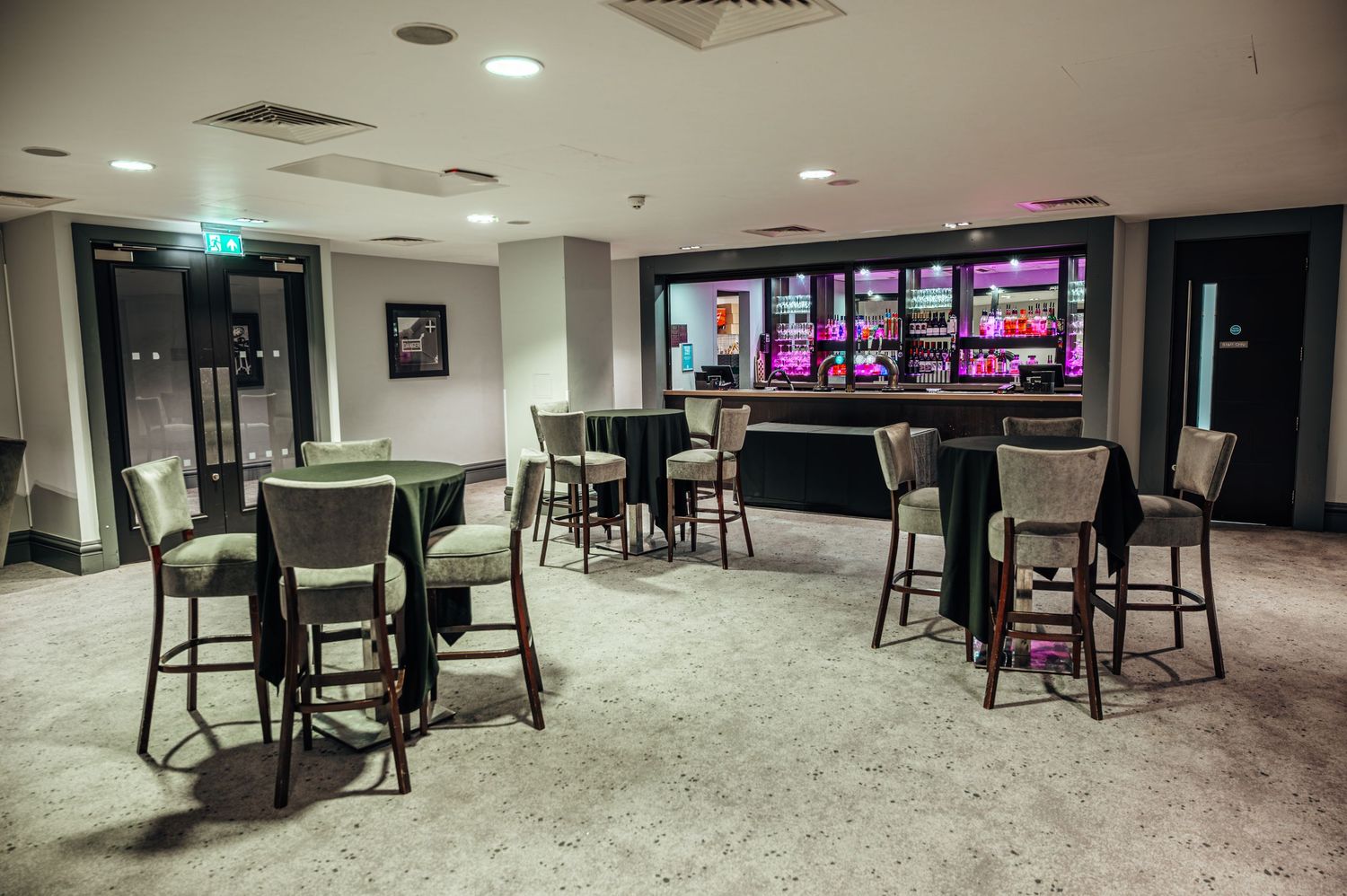 Modern hotel bar lounge with high bar stools, round tables, and a illuminated back bar display in a stylish interior.