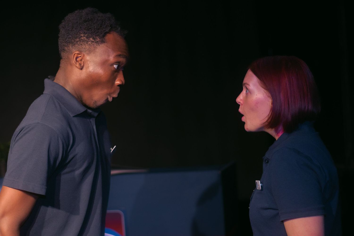 Two staff members in navy uniforms interact during a meeting in front of blue background.