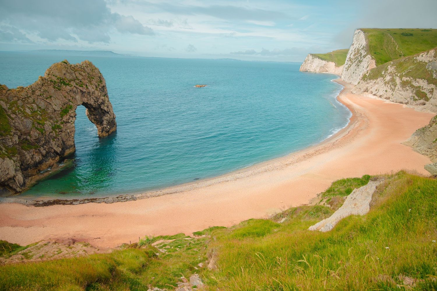 Panoramic coastal view of Durdle Door beach with white cliffs and turquoise waters.