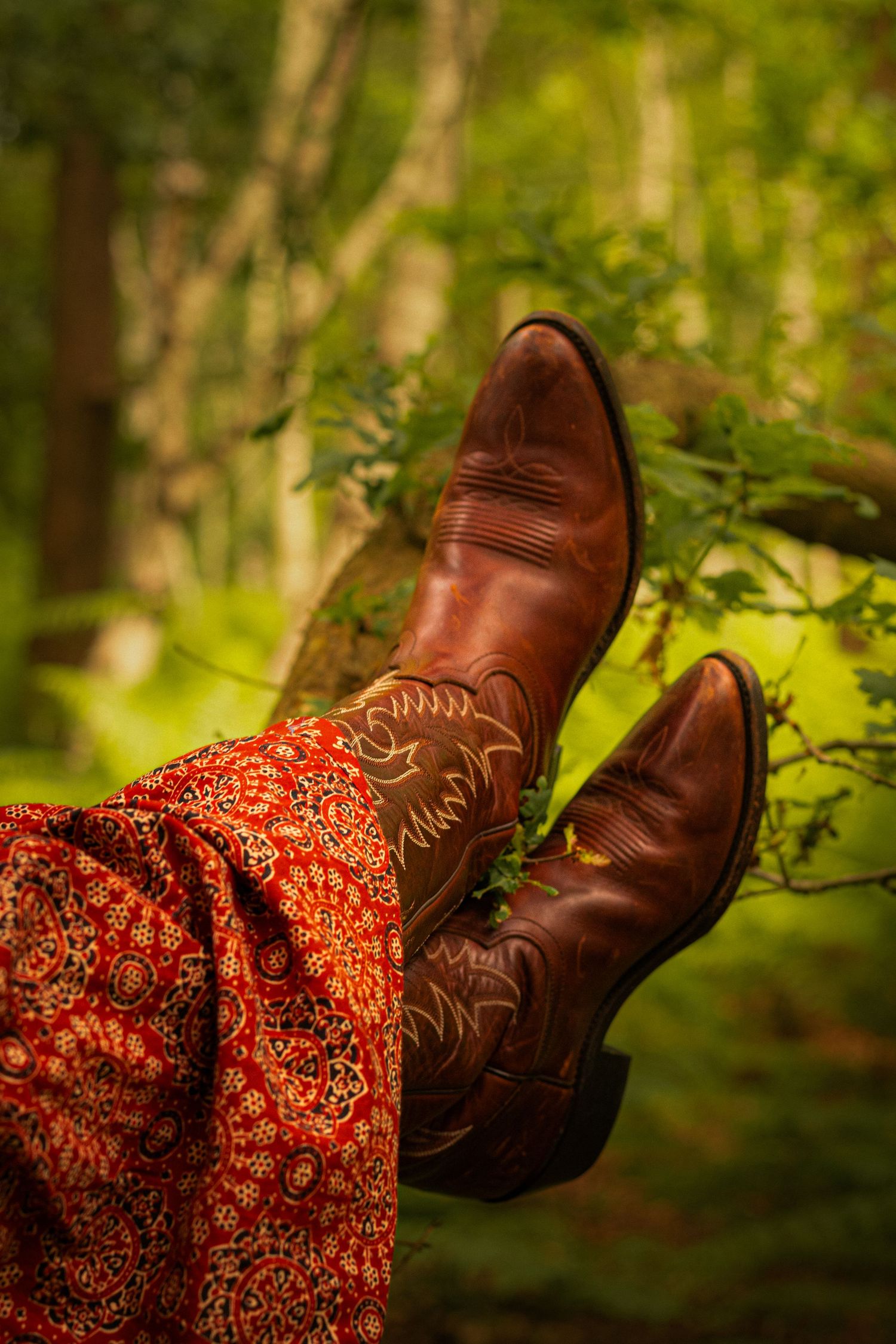 Brown cowboy boots with red floral dress visible in a dreamy forest setting.