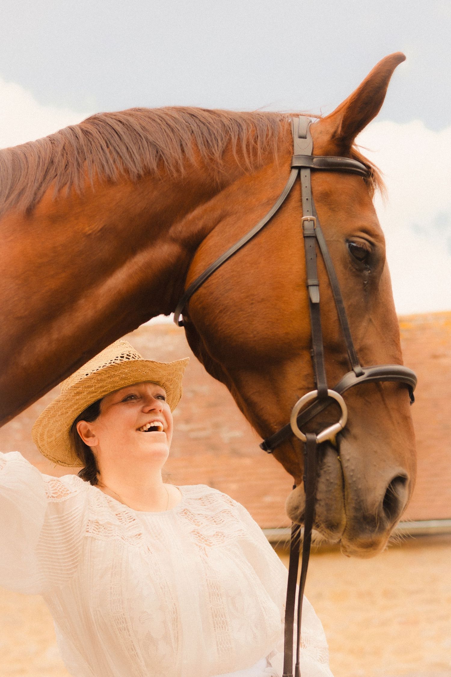 A sun-lit profile shot of a majestic brown horse with someone in white lace and a straw hat.