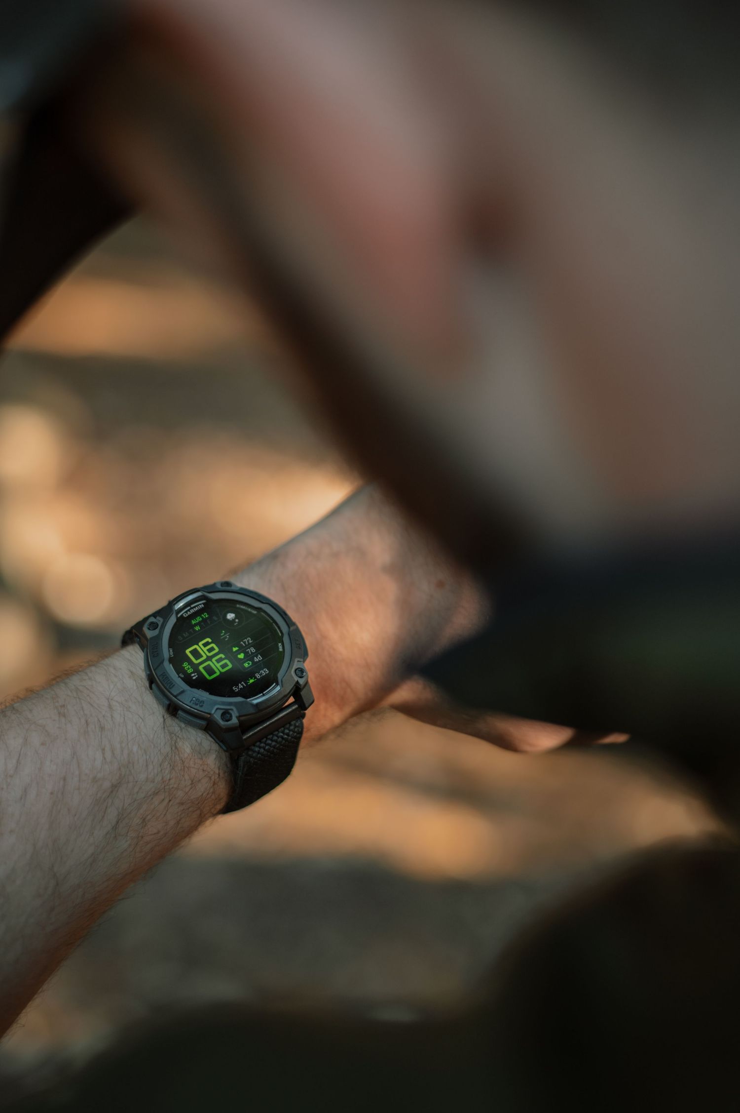 Close-up of a black digital tactical watch with green display on a man's wrist outdoors.
