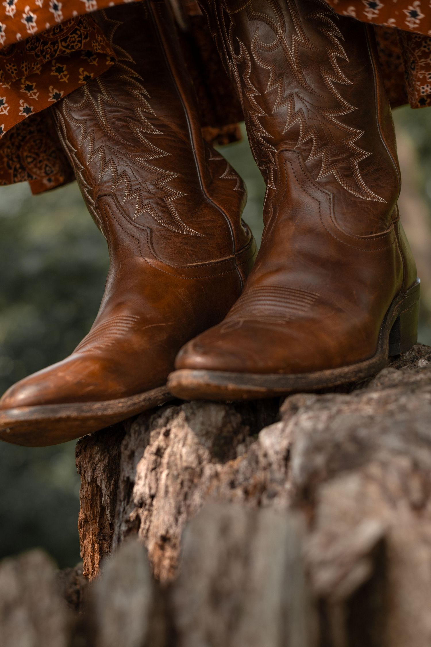 Brown leather cowboy boots rest on a weathered stone surface in rustic lighting.