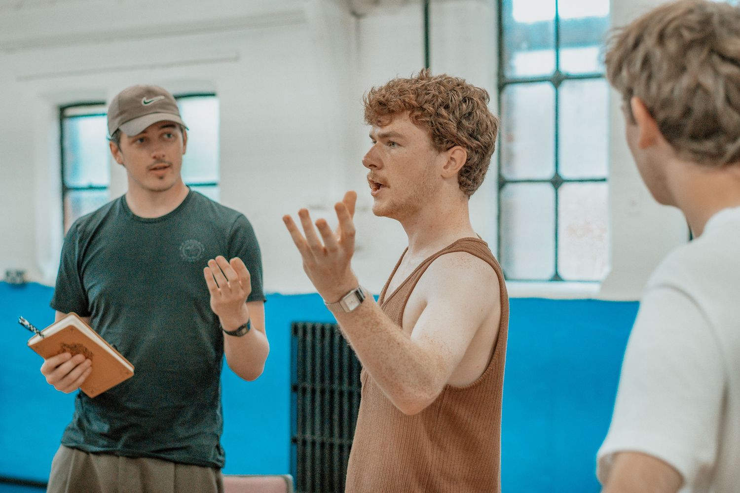 Dance students practice movement exercises in a bright studio with blue walls and wooden floors.