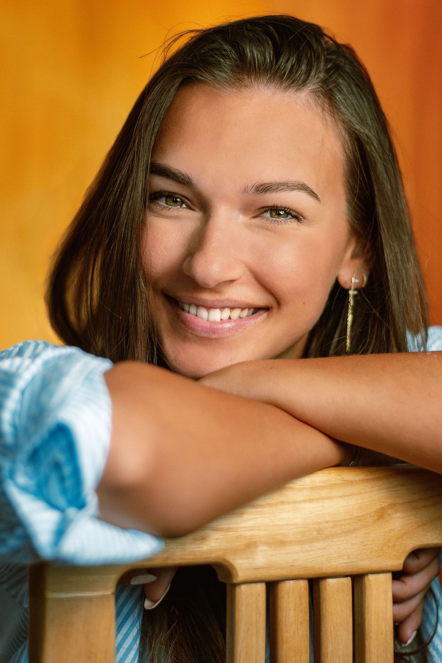 Warm-toned portrait showing joyful expression while leaning on wooden furniture.
