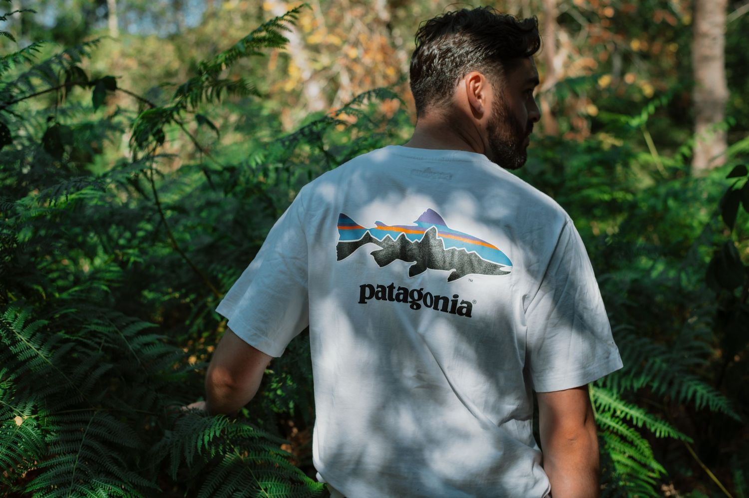 Man wearing a white Patagonia fish graphic t-shirt standing in a lush green forest.
