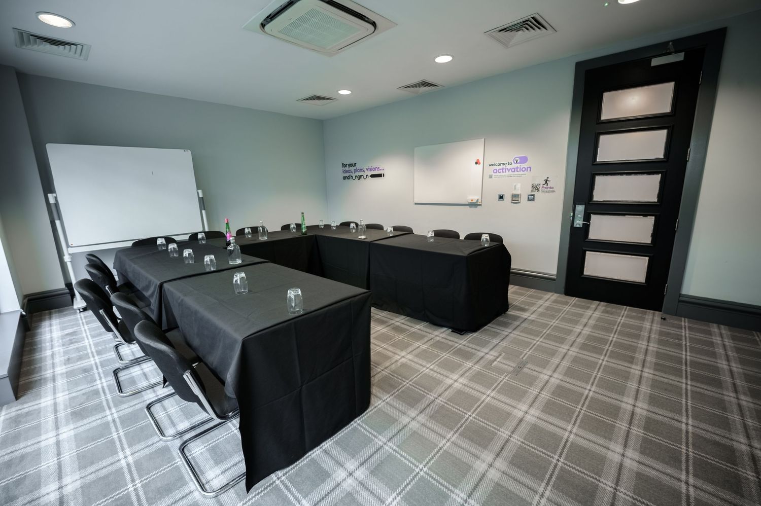 Modern conference room with U-shaped table setup, whiteboard, and plaid carpet flooring in a professional meeting space.