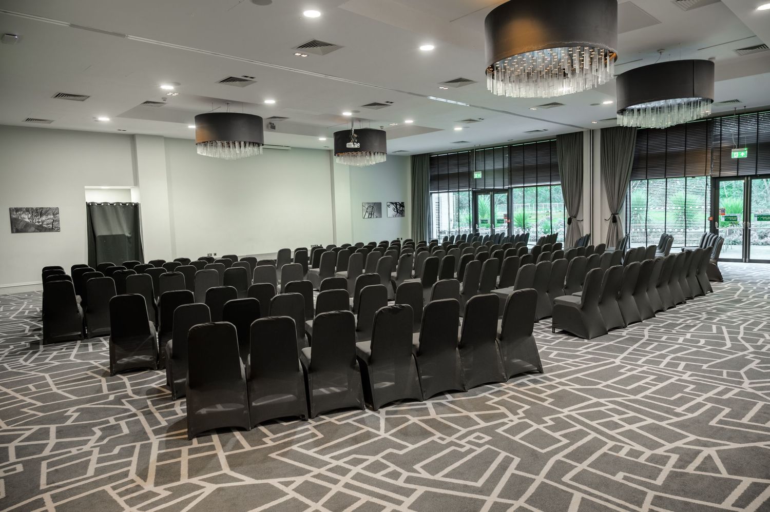 Elegant conference room with rows of black chairs, patterned carpet, and modern chandeliers in a bright event venue.