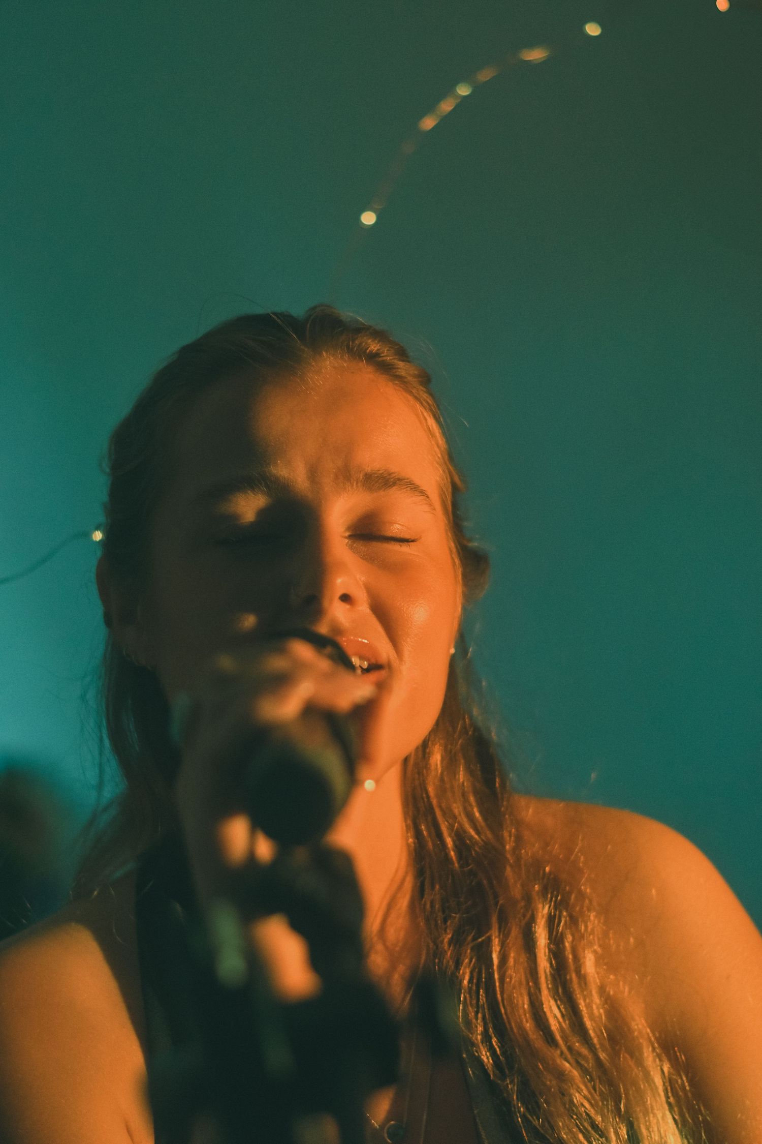 Close-up profile shots of person singing in dramatic teal-tinted lighting.