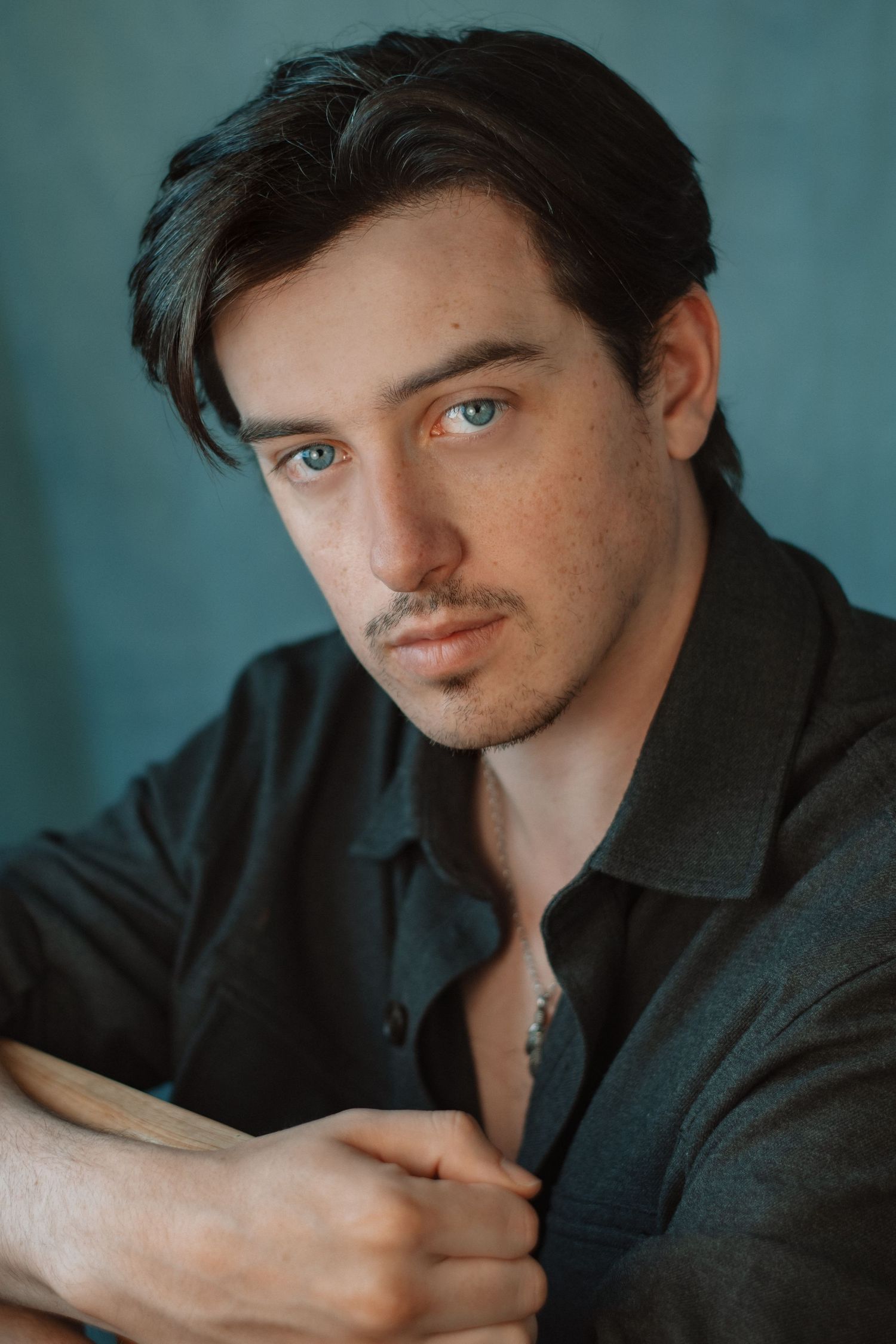 Moody portrait series against a teal backdrop with dark clothing.
