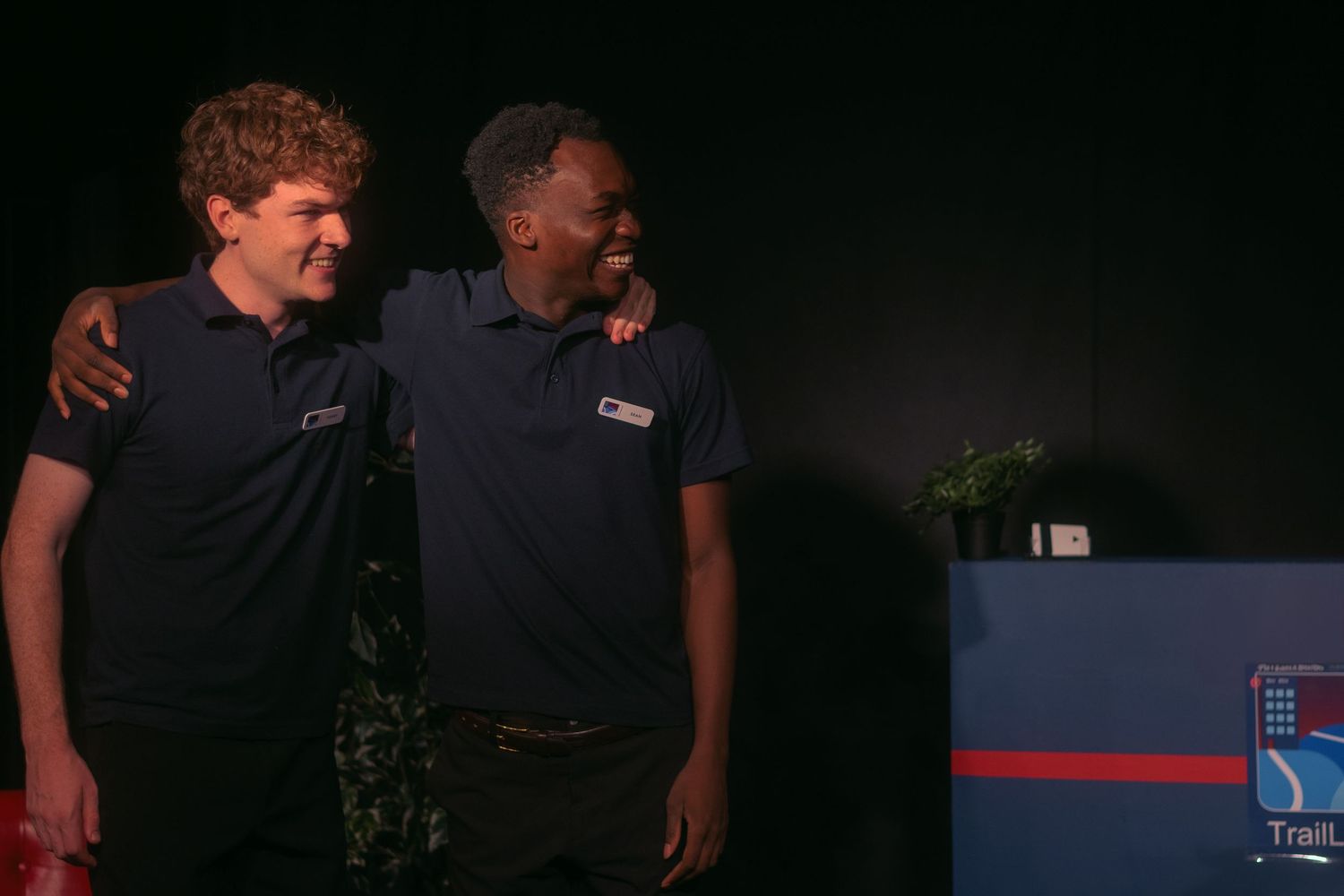 Two colleagues wearing blue polo shirts stand together at night during an event.