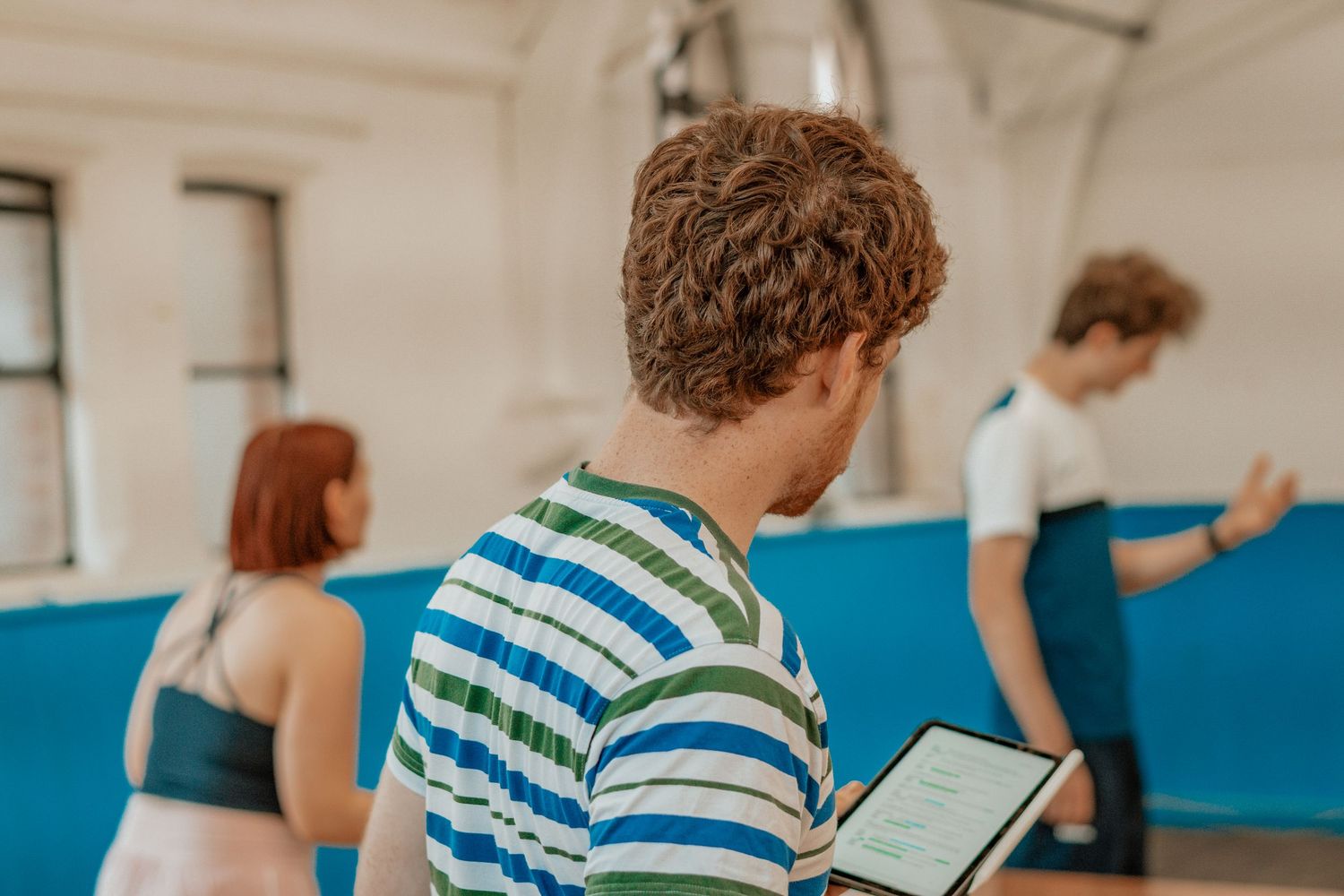 Person reading from digital tablet in striped shirt with others in background.