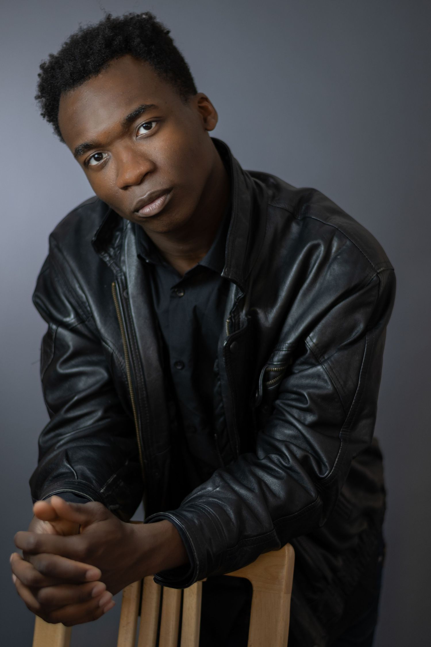 Professional portrait series in black leather jacket against gray backdrop.