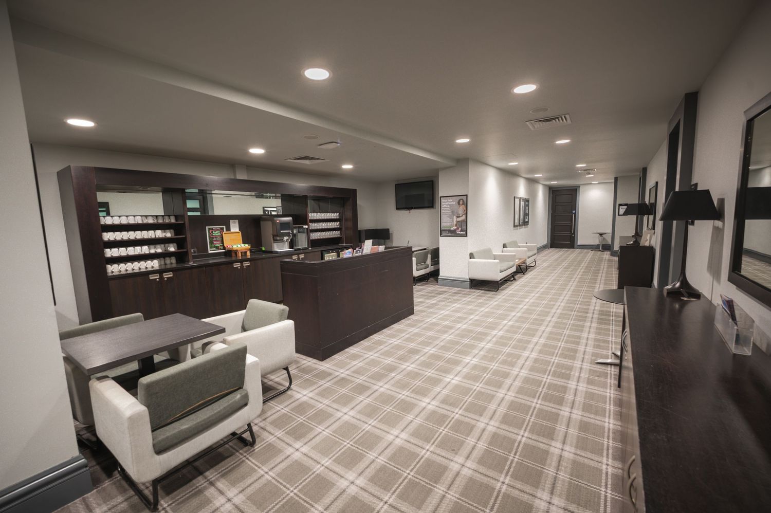 Modern hotel lobby with plaid carpet, reception desk, white chairs, and product display shelving in a neutral gray color scheme.