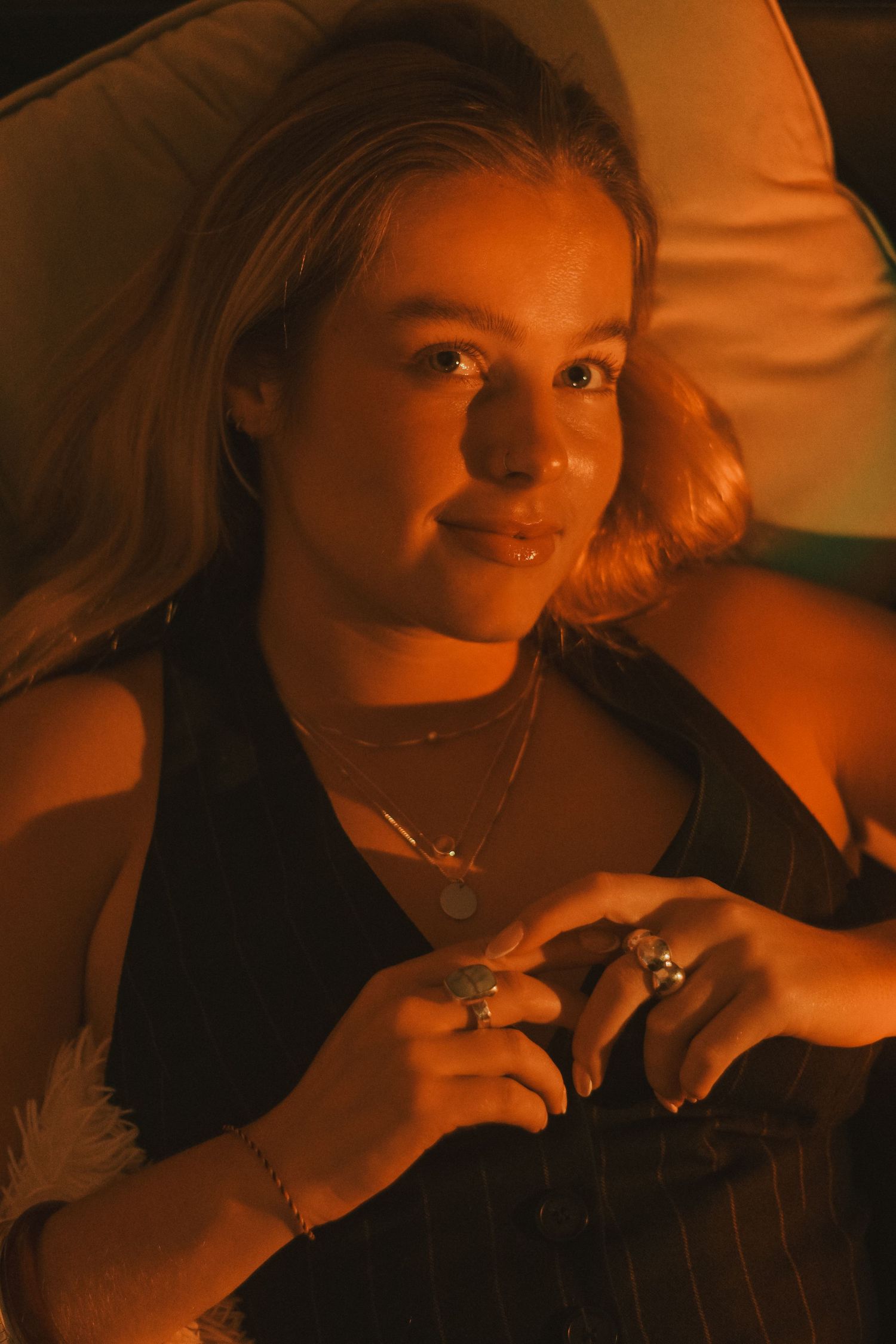 Person in black top with jewelry relaxing on couch in warm lighting.