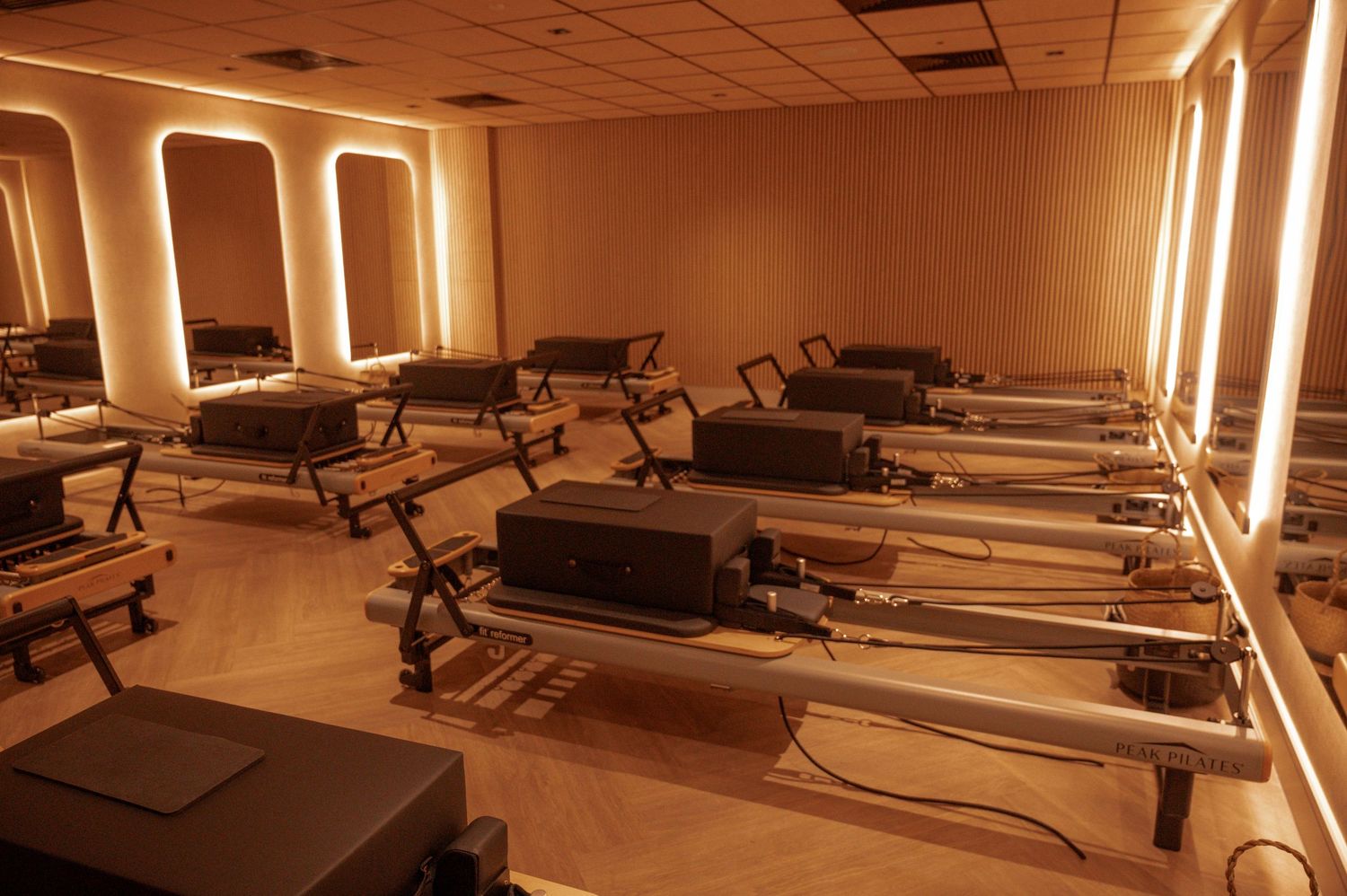 Pilates studio with reformer machines arranged in rows, warm amber lighting, and large mirrors on the walls.