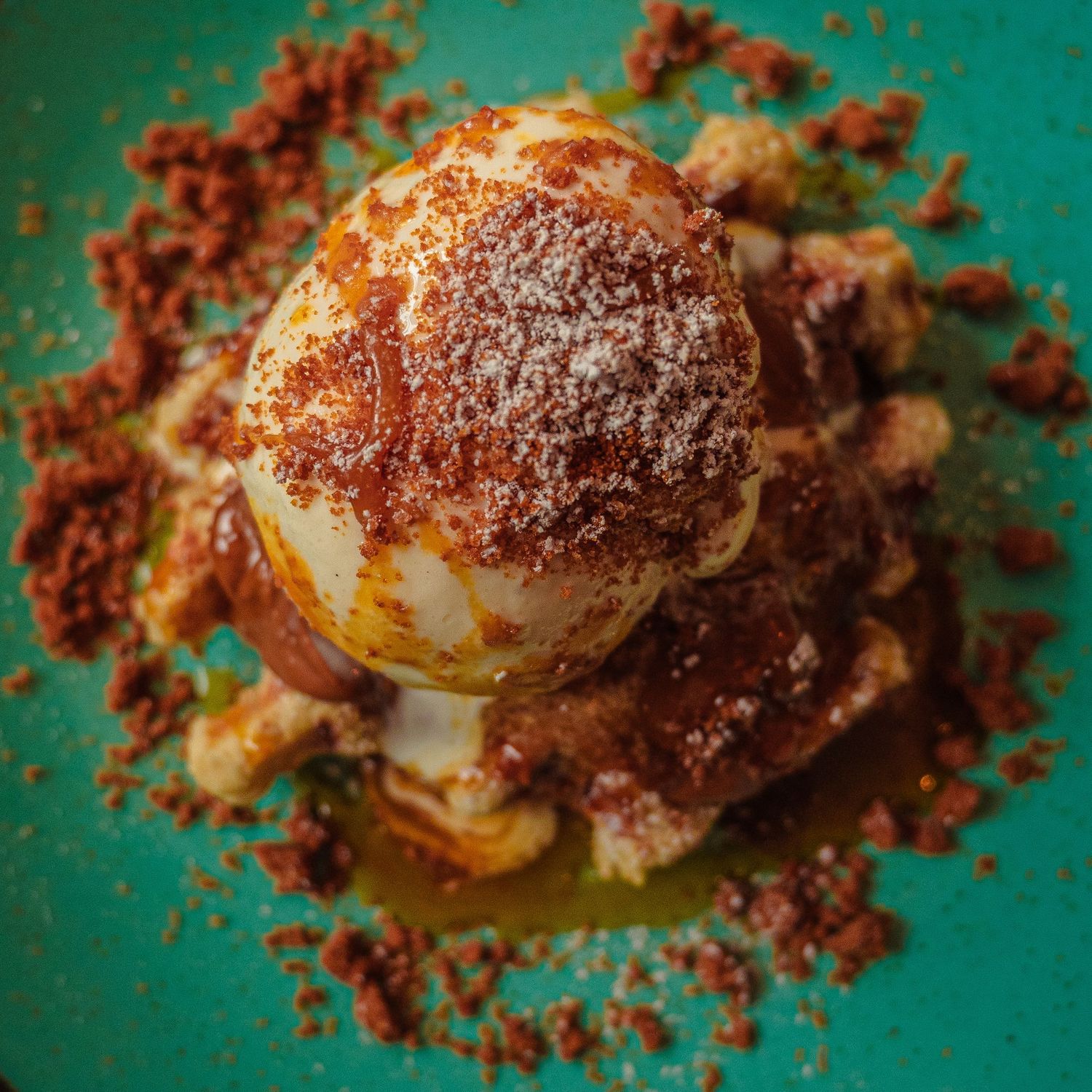 Dessert presentation on turquoise plate with crumbled chocolate and caramel sauce.